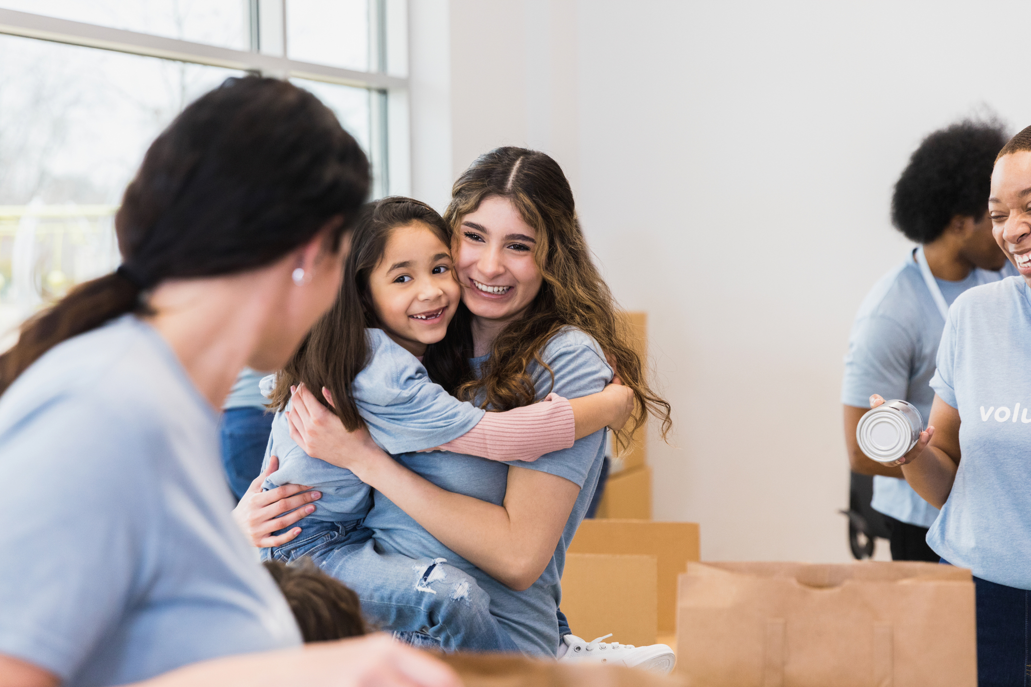 Young adult aunt hugs elementary age niece at food drive