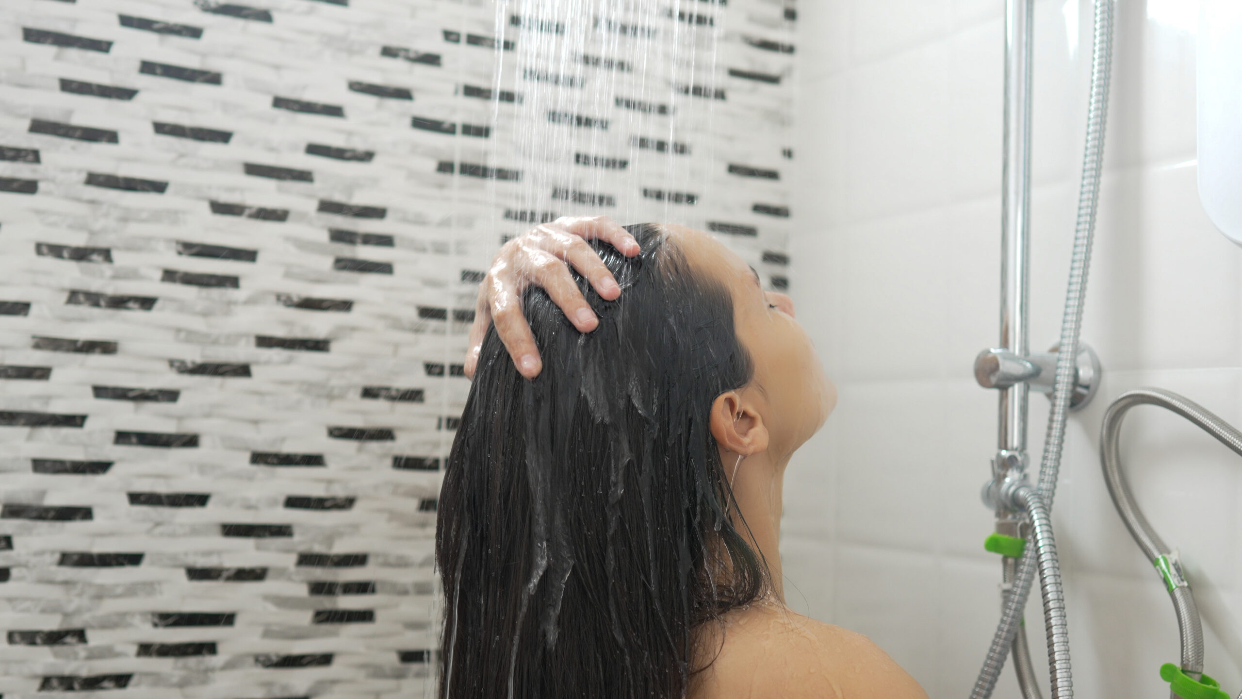 Young woman taking a shower and washing her hair in the bathroom