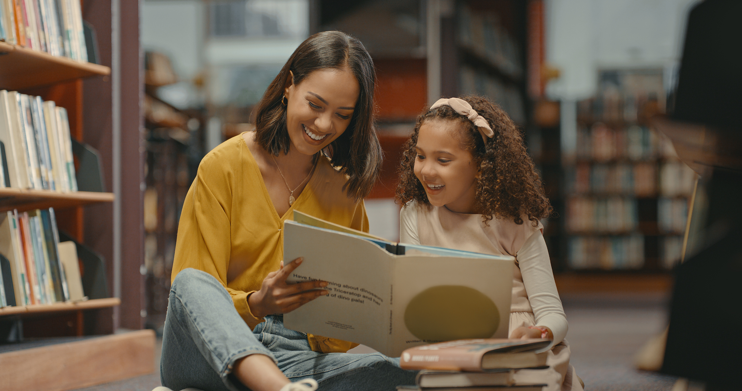 Teacher helping a young student with her homework in the library after school. Two females are reading a book together in the bookstore. They are doing research for a project