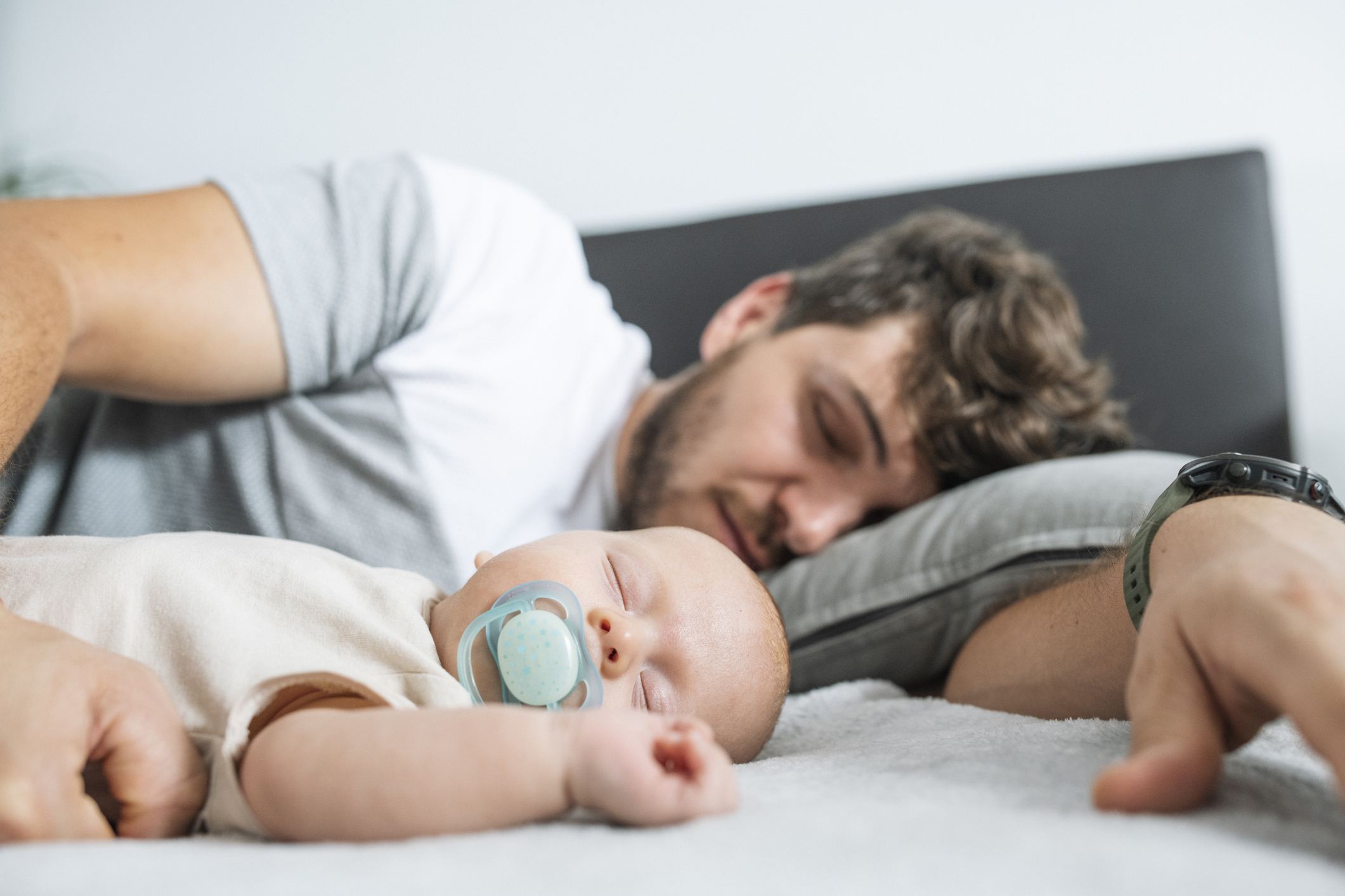 Young father sleeping beside baby son.
