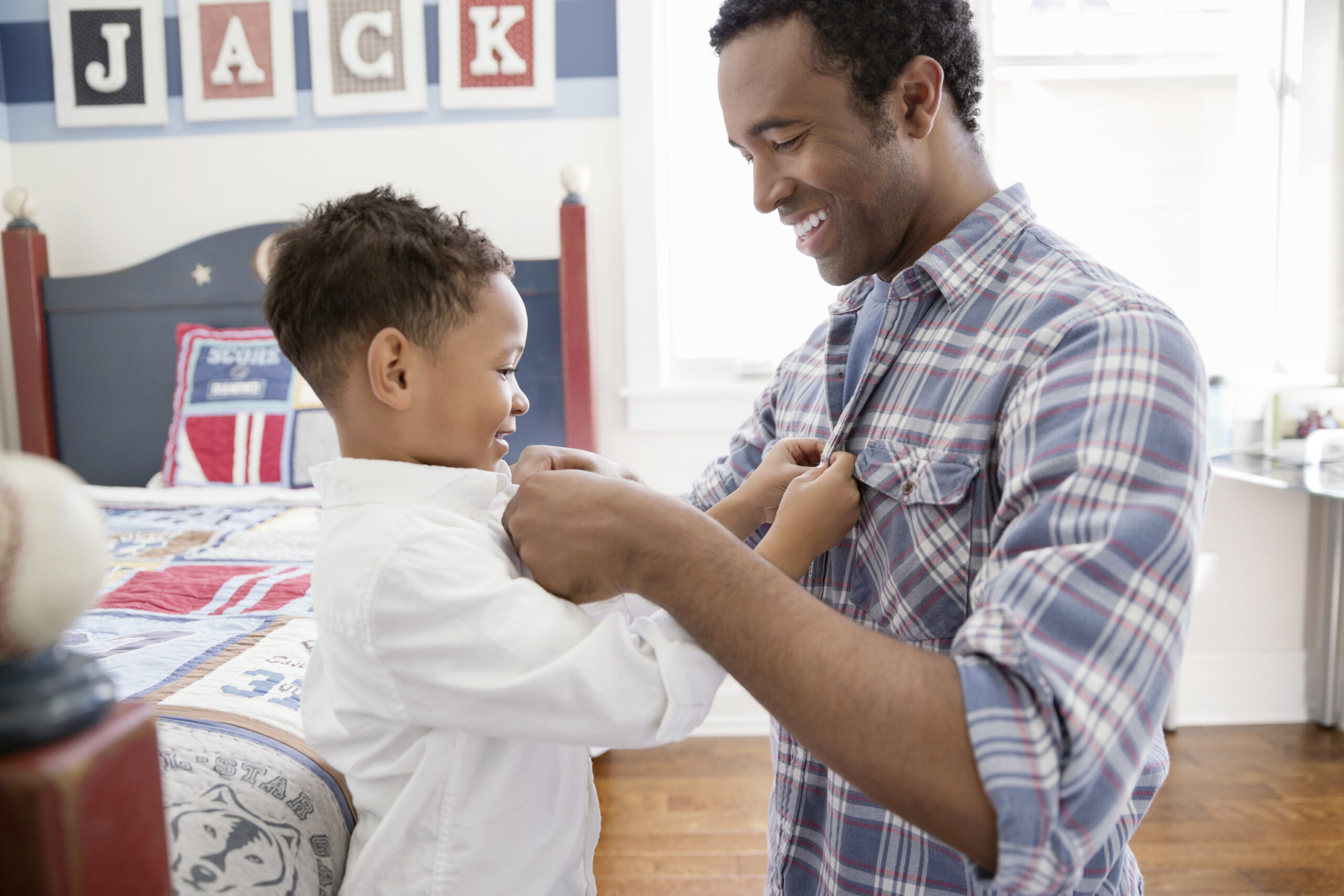 Happy father and son buttoning each others shirts in bedroom