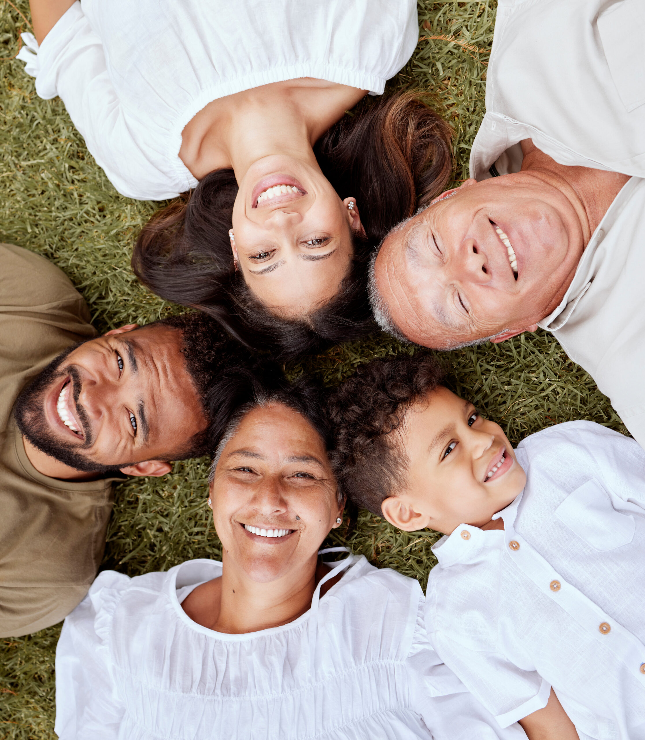 Big family, face and portrait smile above relaxing in quality bonding time together on the grass in the outdoors. Happy family smiling in joyful happiness lying in relax for summer break in the park