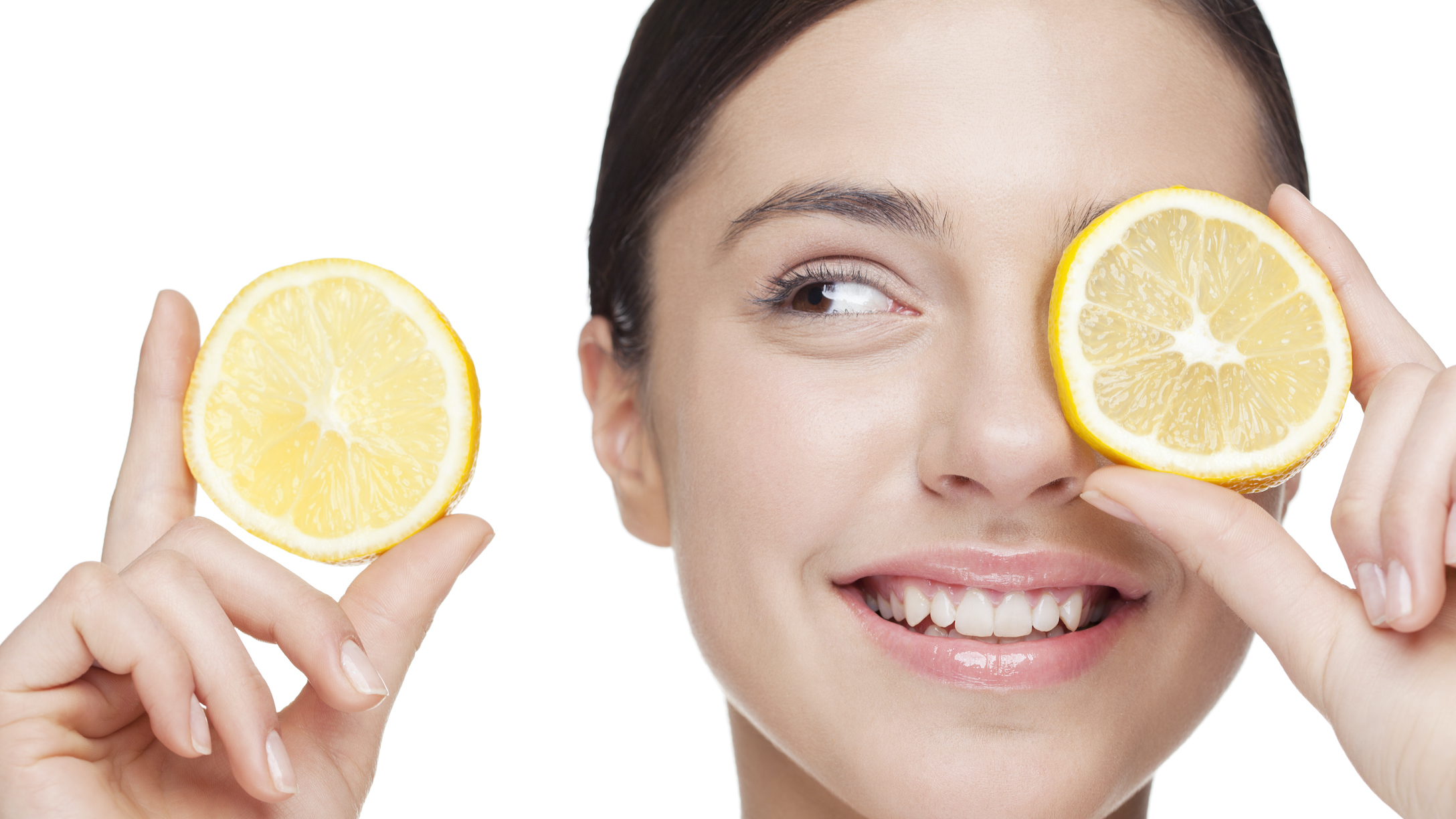 A woman holding a slice of lemon over her eye