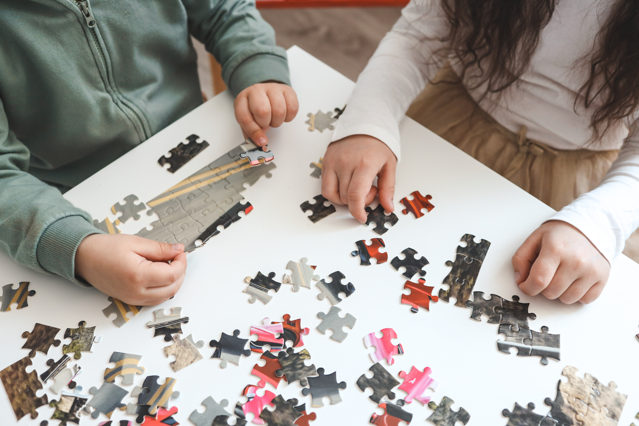 Brother and sister playing puzzles at home. Children connecting jigsaw puzzle pieces in a living room table. Kids assembling a jigsaw puzzle. Fun family leisure