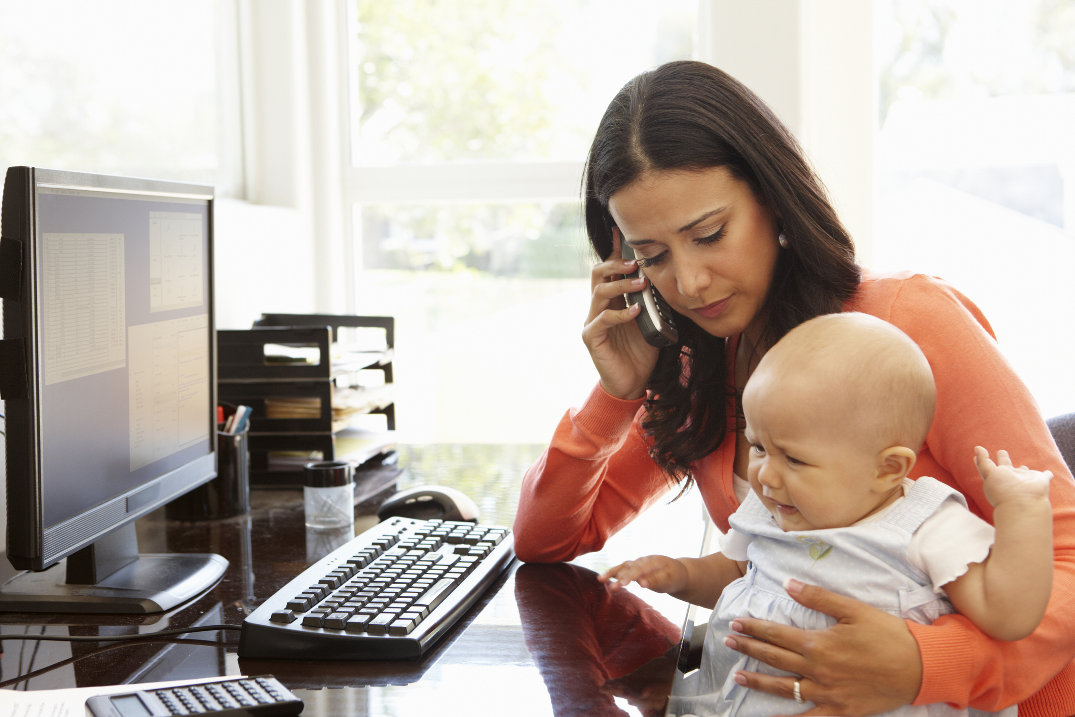 Hispanic mother with baby working in home office