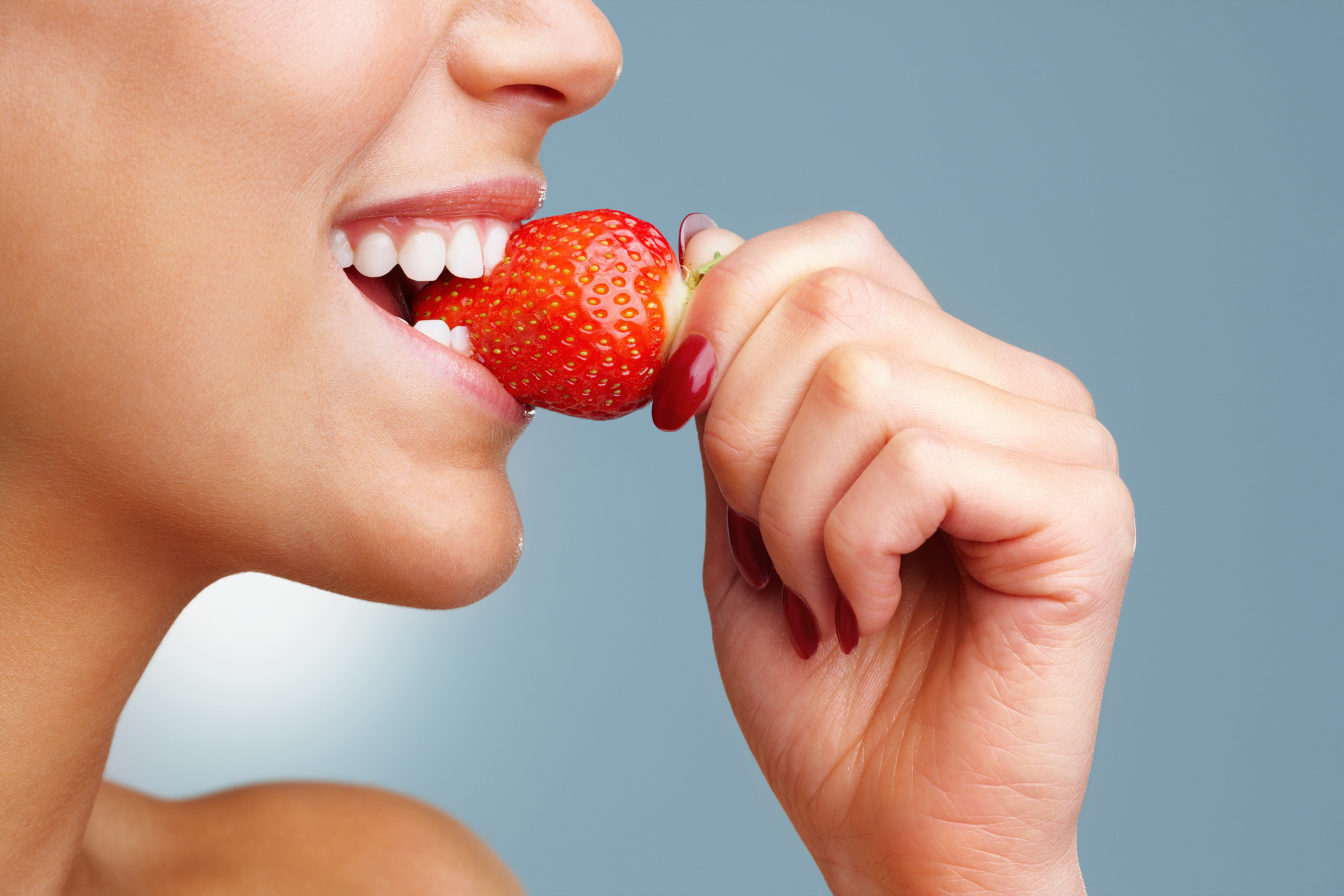 Macro view of a pretty young female eating fresh strawberry