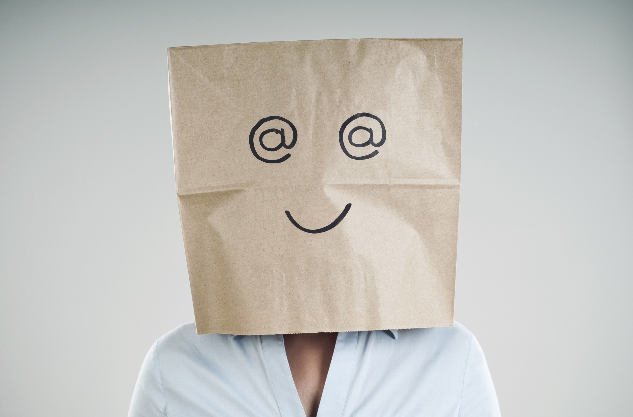 Person wearing a paper bag with @ symbol eyes and a smile