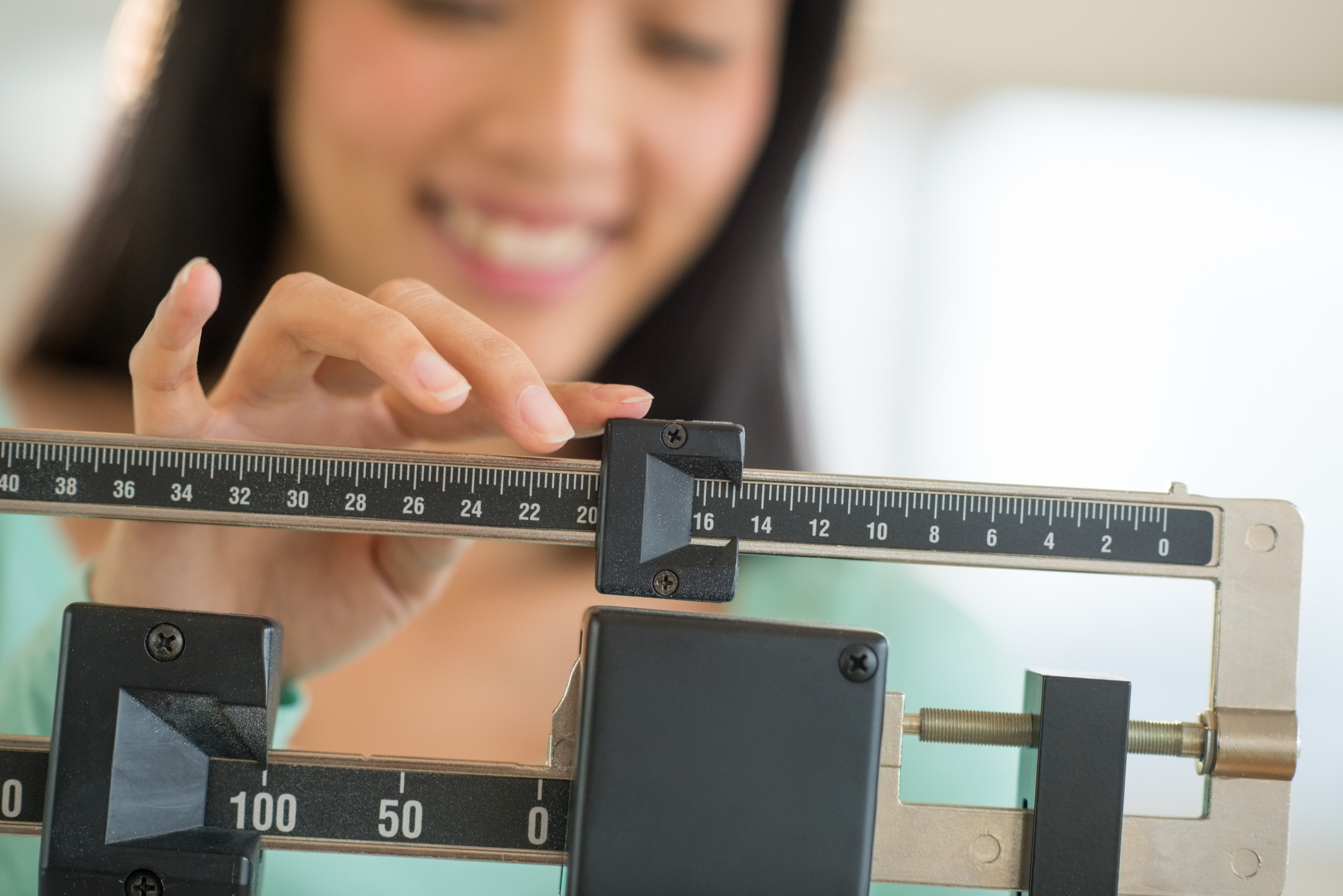 Smiling young Asian woman adjusting a weight scale