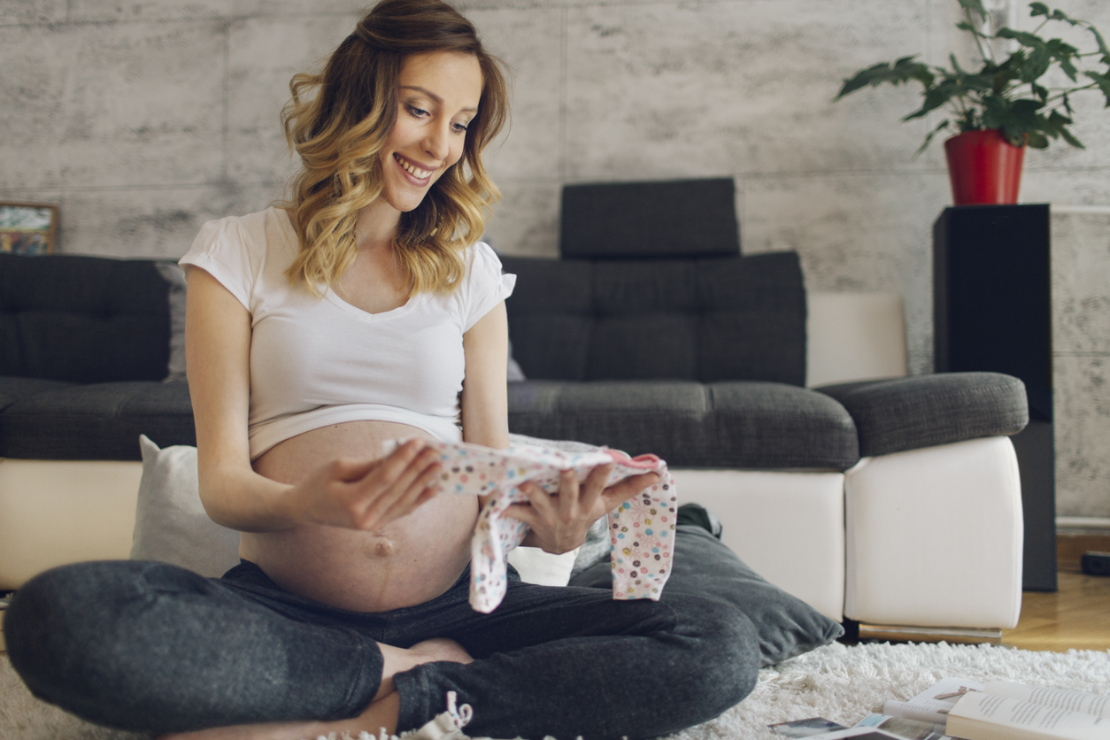 Pregnant Woman Looking At Baby Clothes.