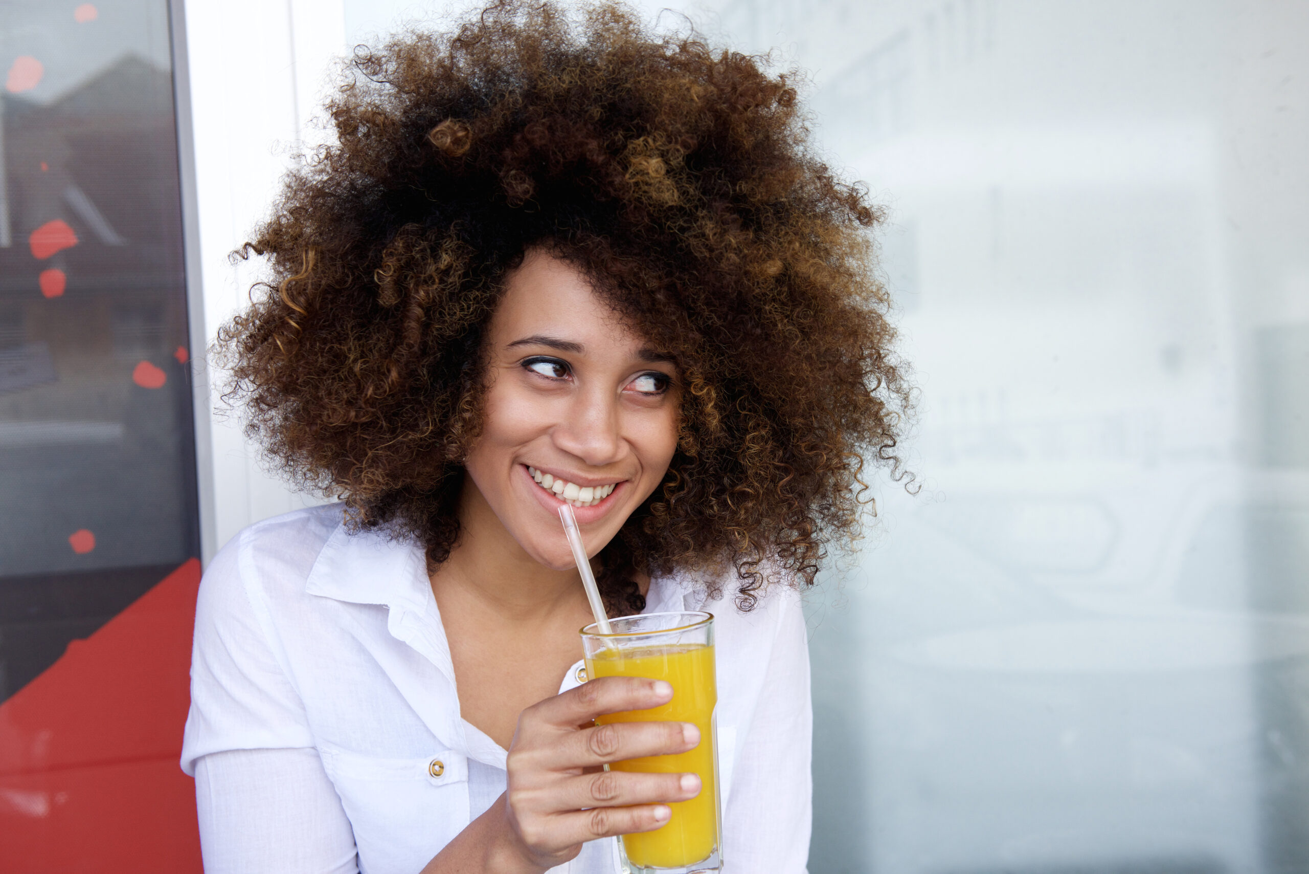 Smiling young african woman drinking juice at outdoor cafe