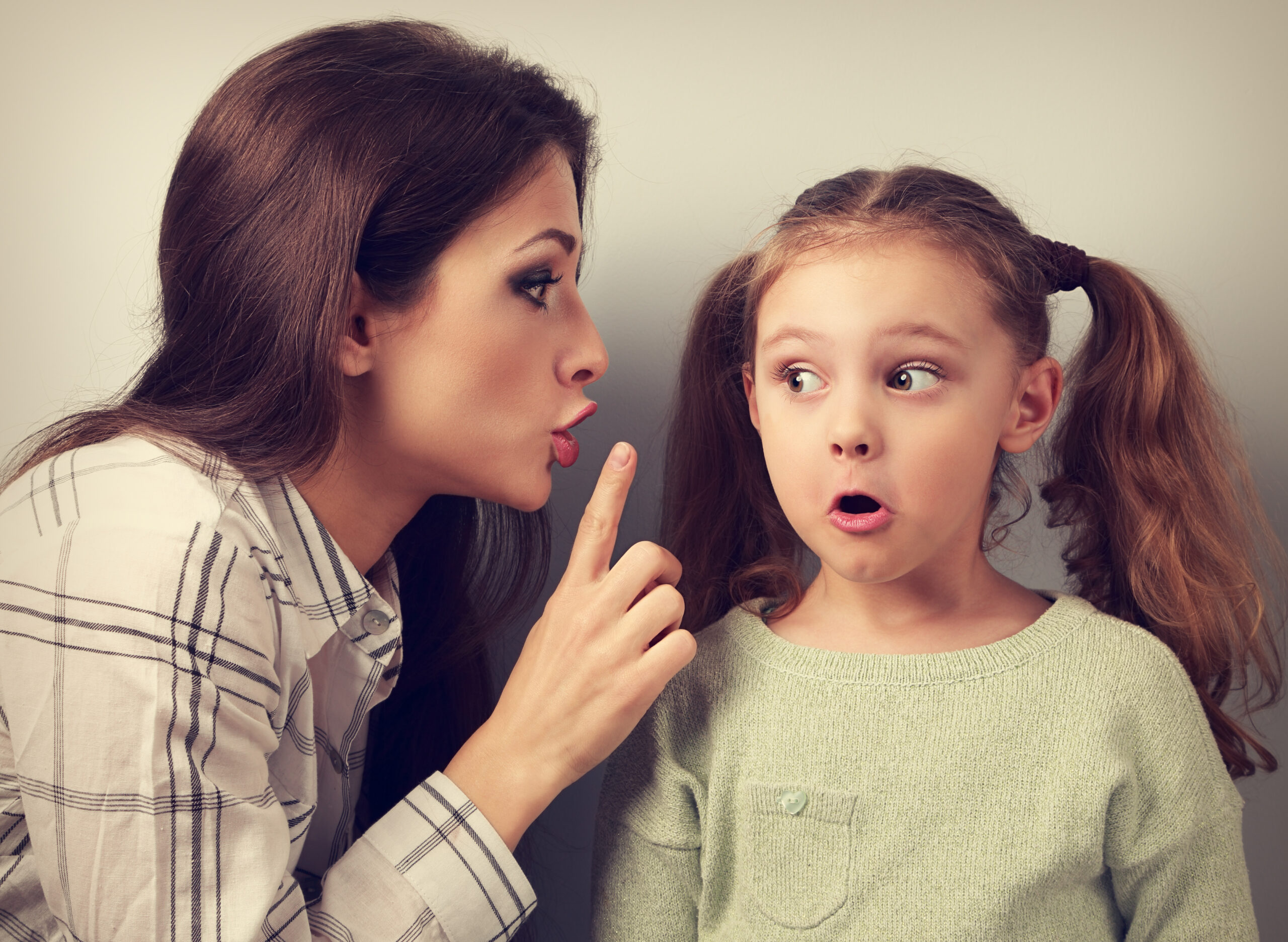 Young mother showing finger the silence sign to her kid