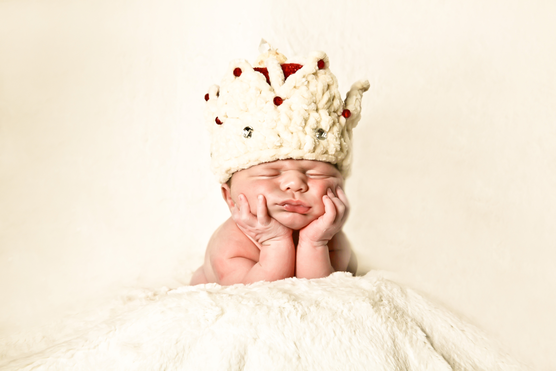 Newborn baby wearing a crown sleeping on his hands