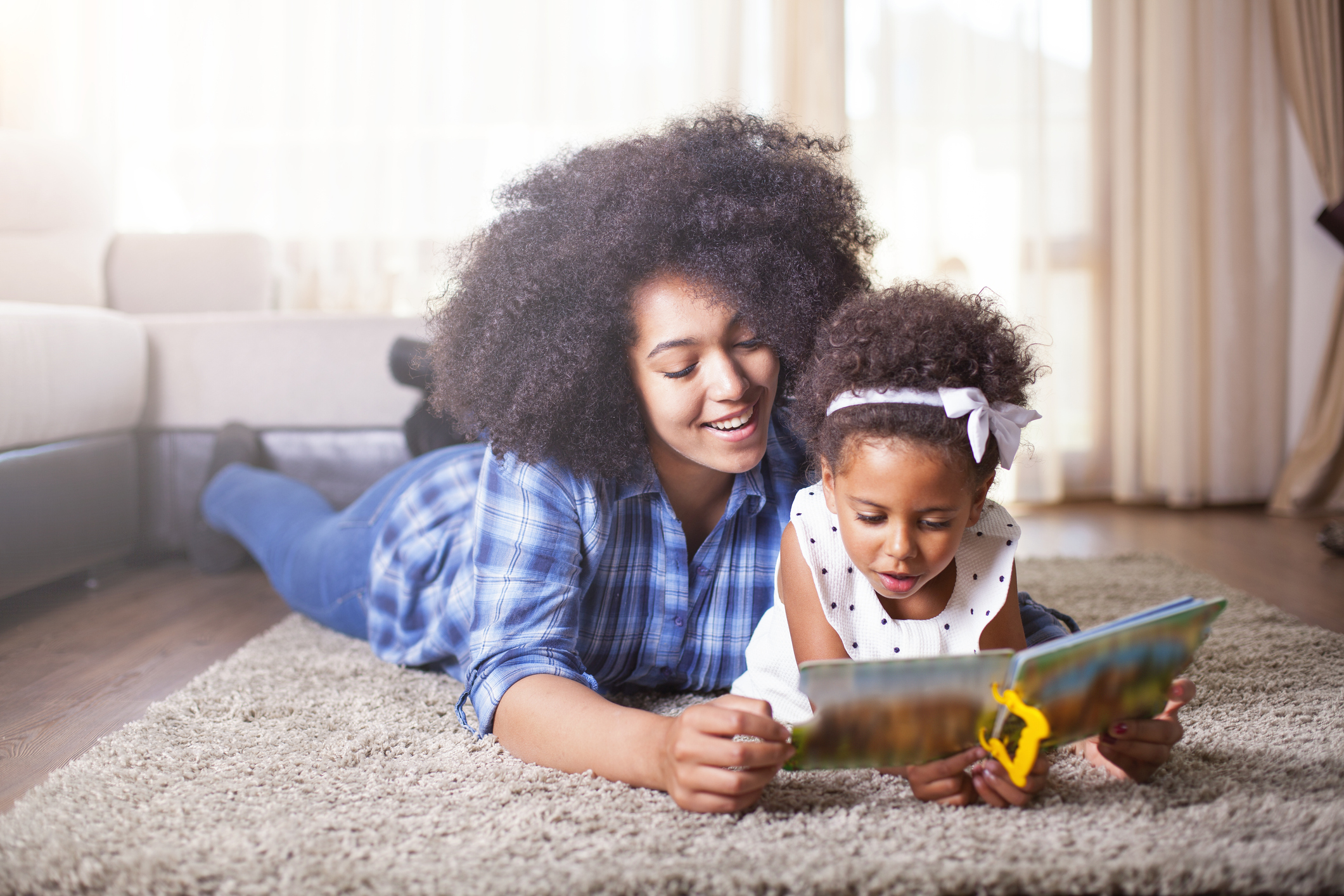 Mother reading a book to her daughter on carpet