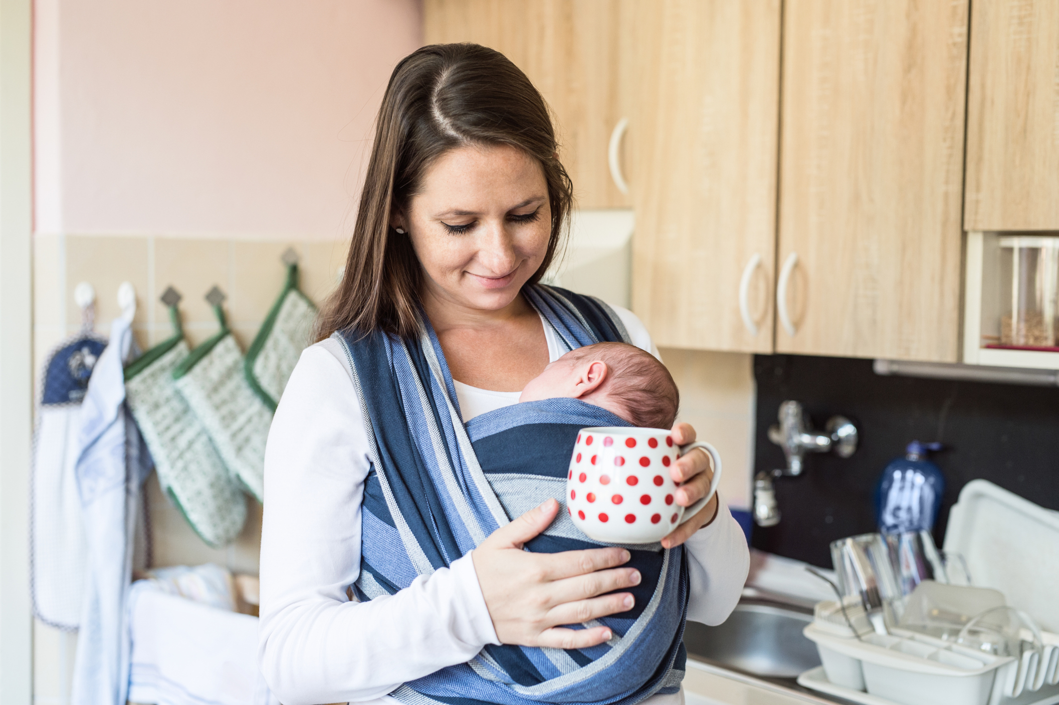 Young mother in kitchen with her son in sling