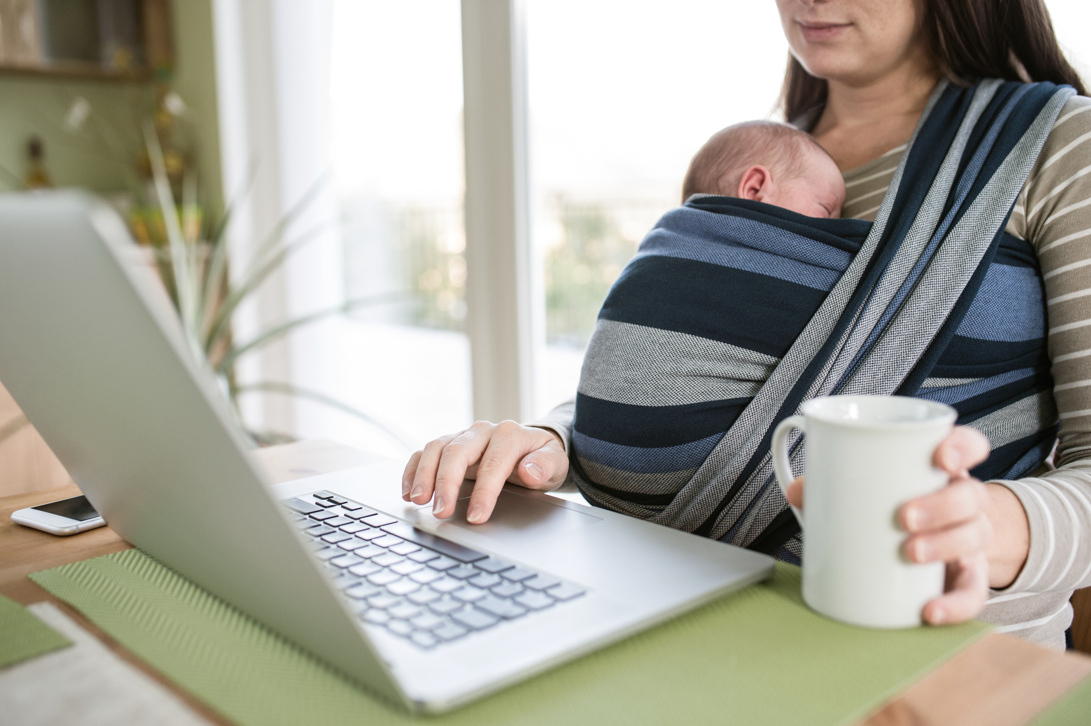 Unrecognizable mother with son in sling, writing on notebook