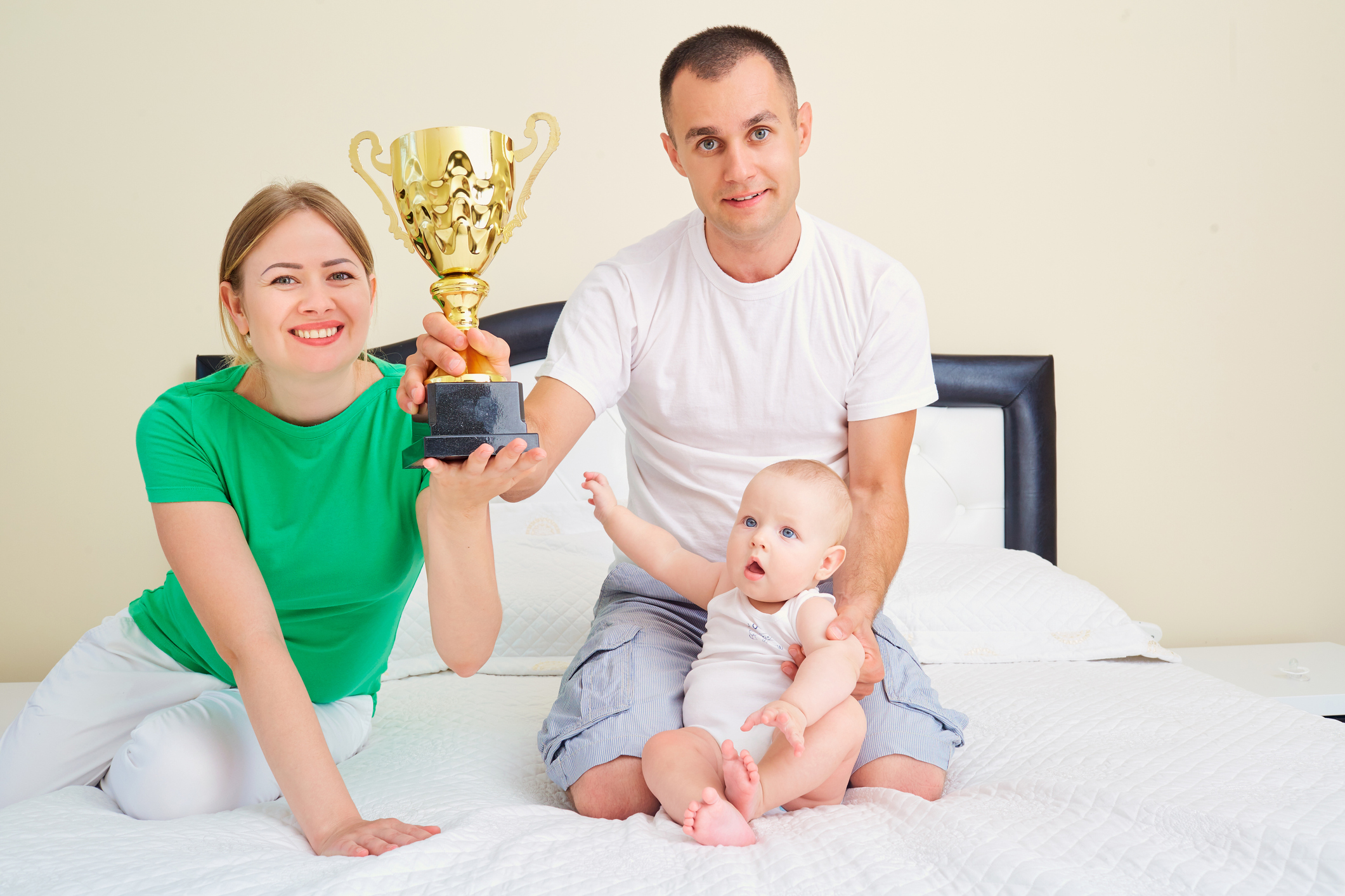 Mother, father and baby with the cup champion  bed togethe