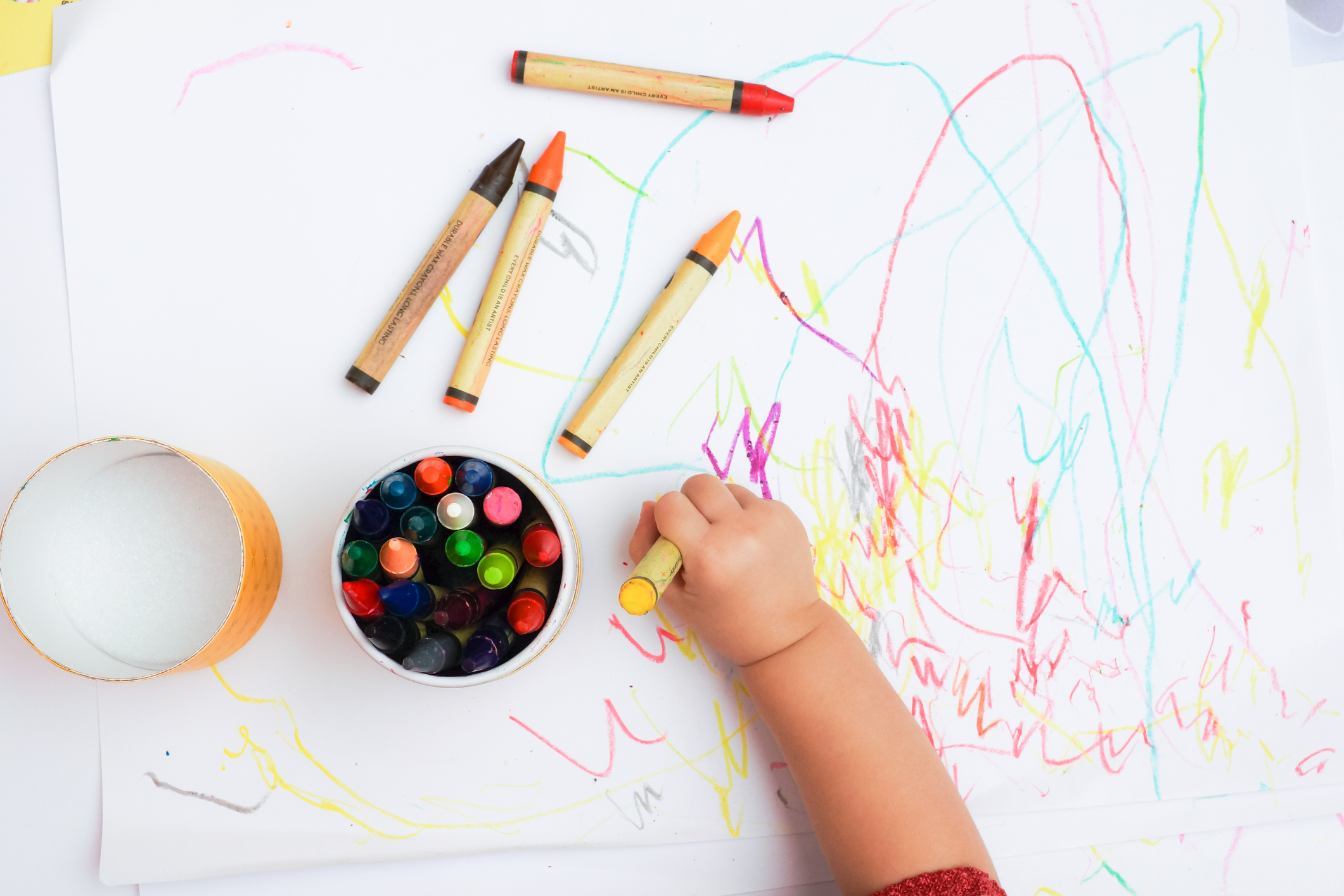 Baby's hand drawing on the white paper with colorful crayons