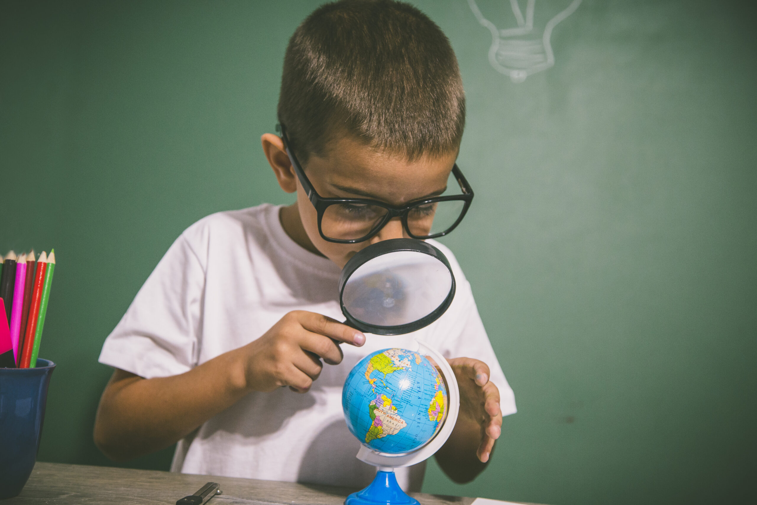 Boy looking through magnifying glass at globe