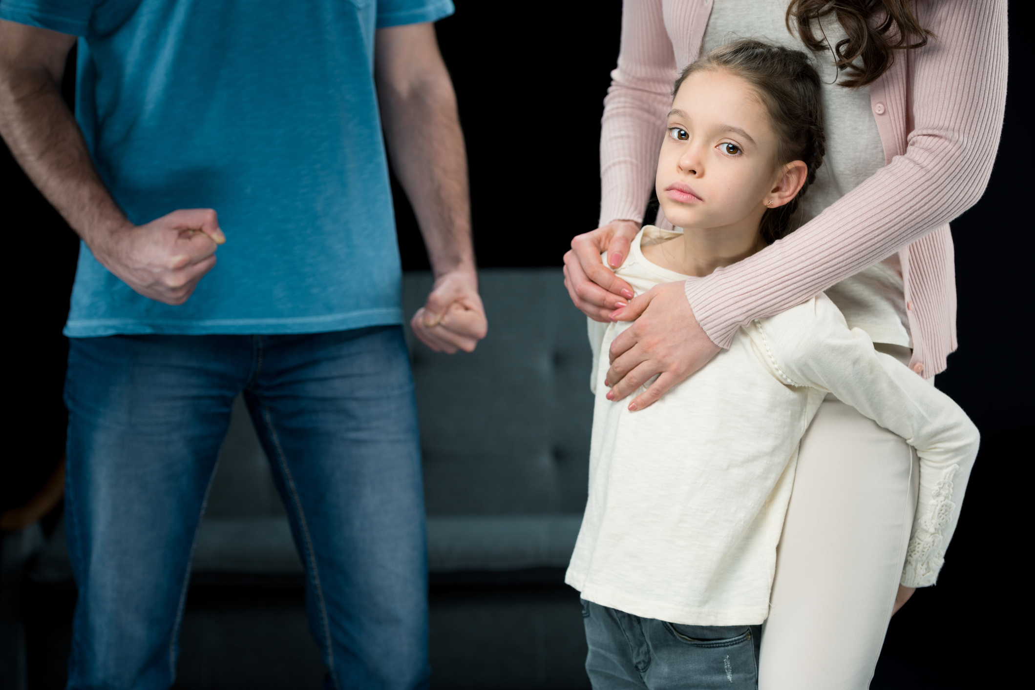 portrait of daughter hugging mother with aggressive father behind