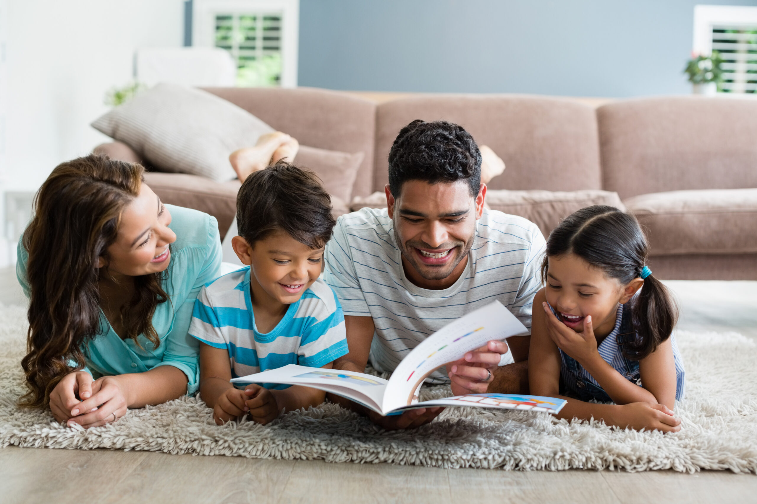 Parents and children lying on rug and reading book in living room