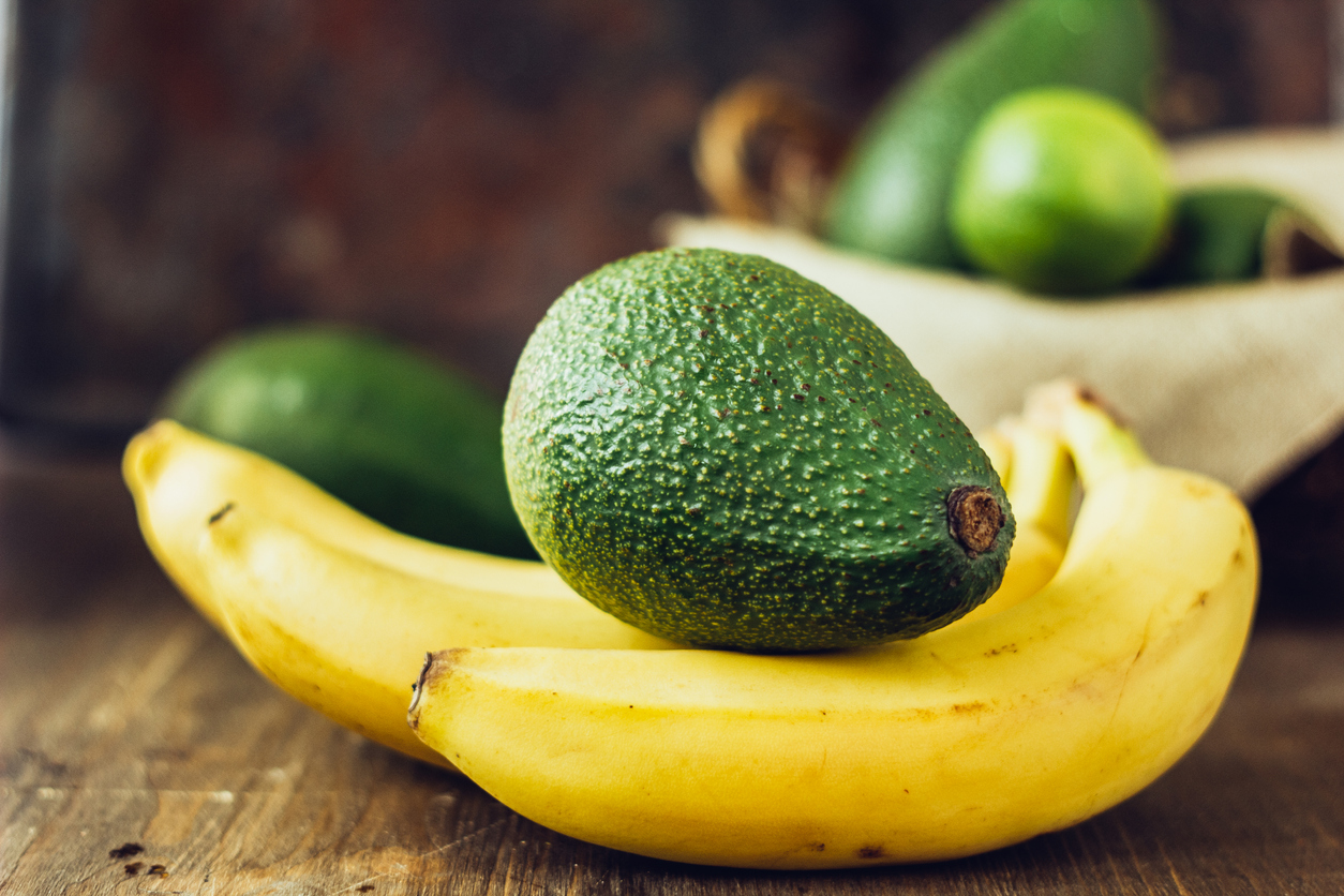 Avocado and banana over brown wooden background.