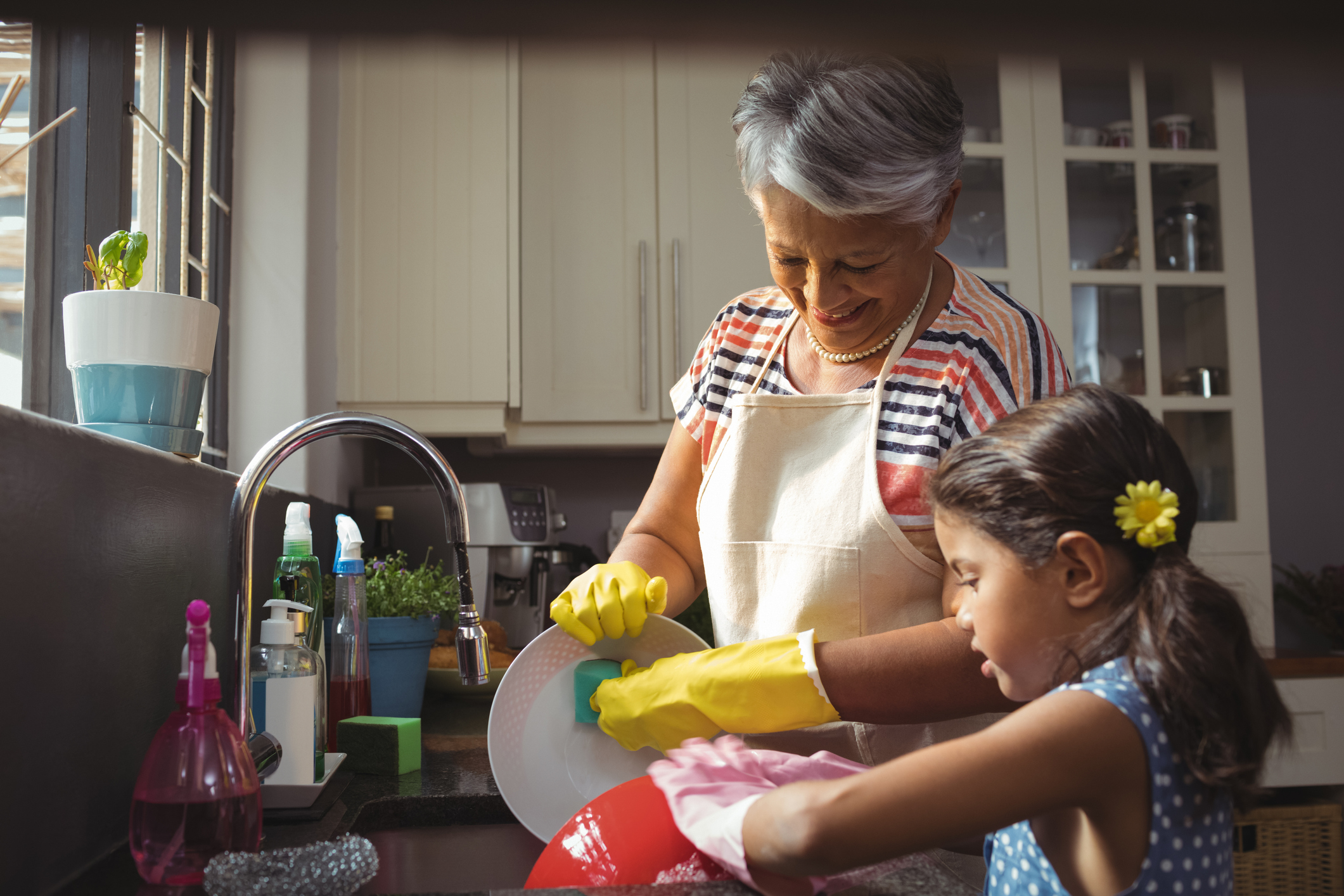 Grandmother and granddaughter washing utensil in kitchen sink