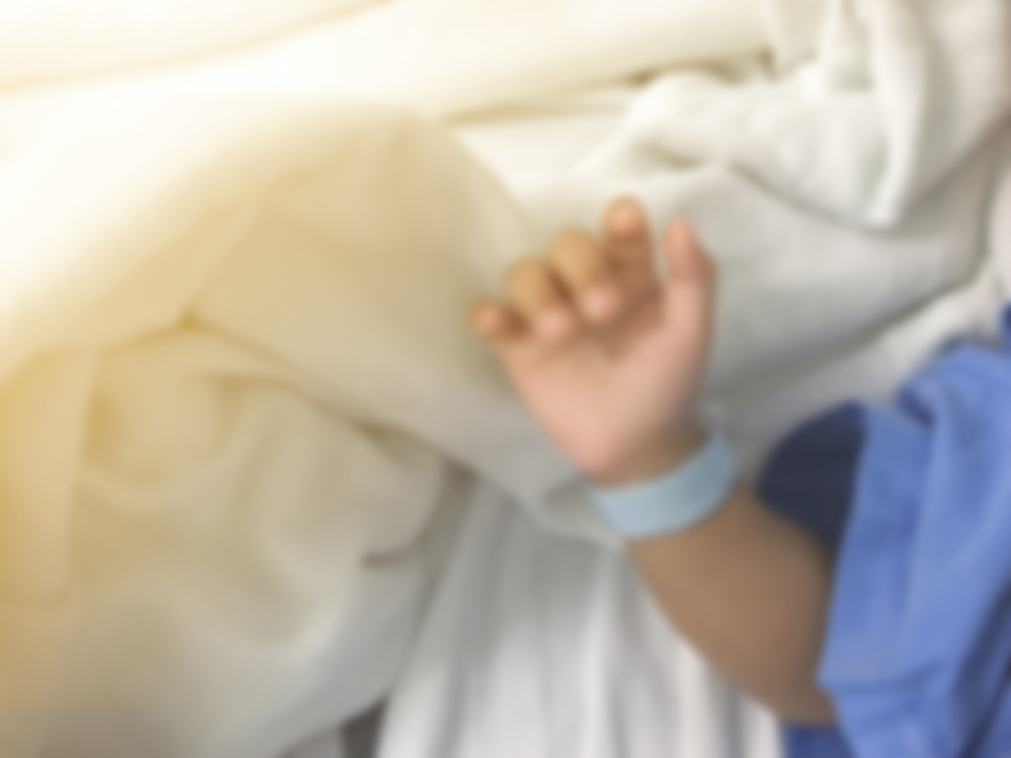 Blurry background of illness hand kid with name tag bracelets on bed in hospital