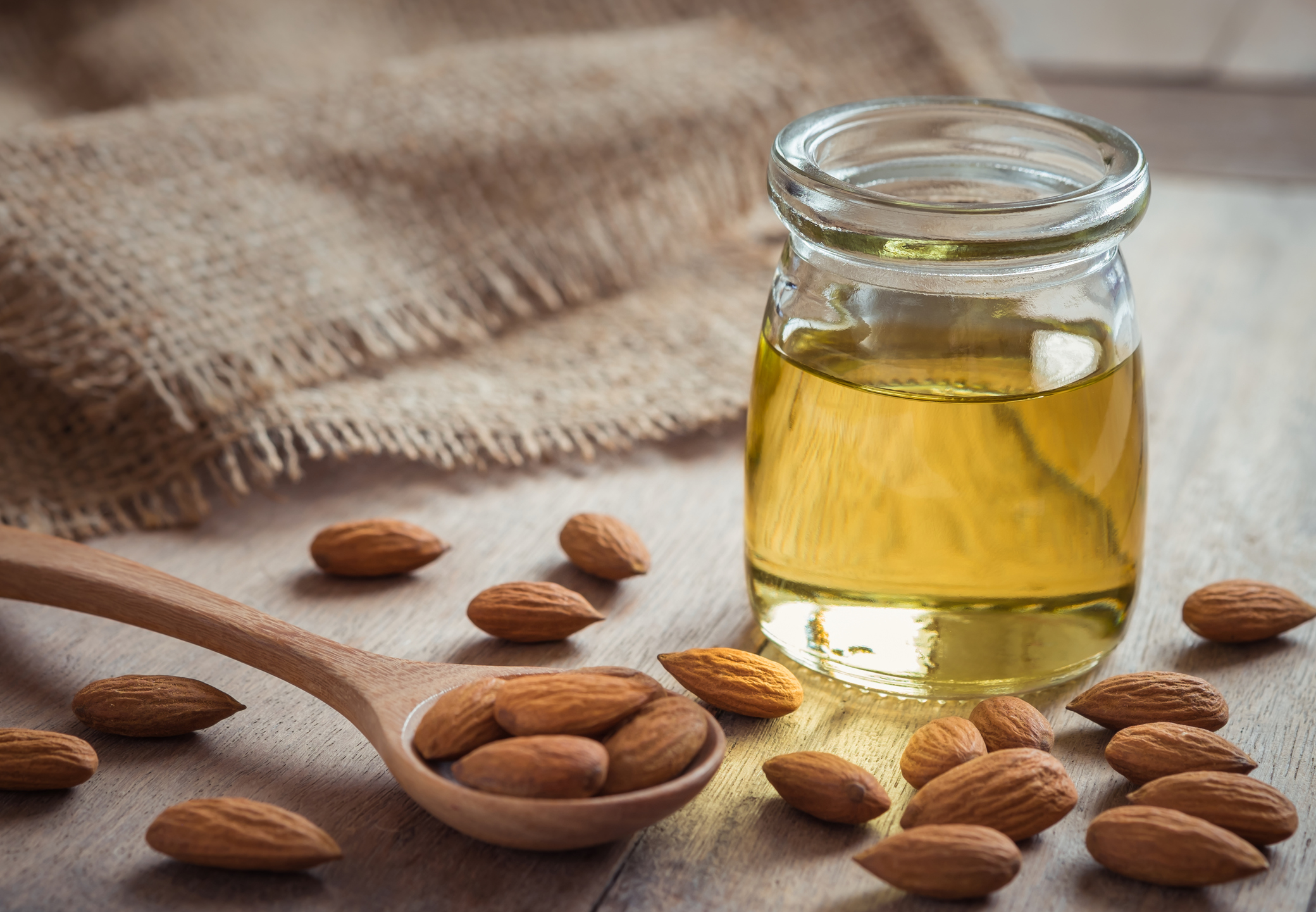 Almond oil in glass bottle and almonds on wooden table