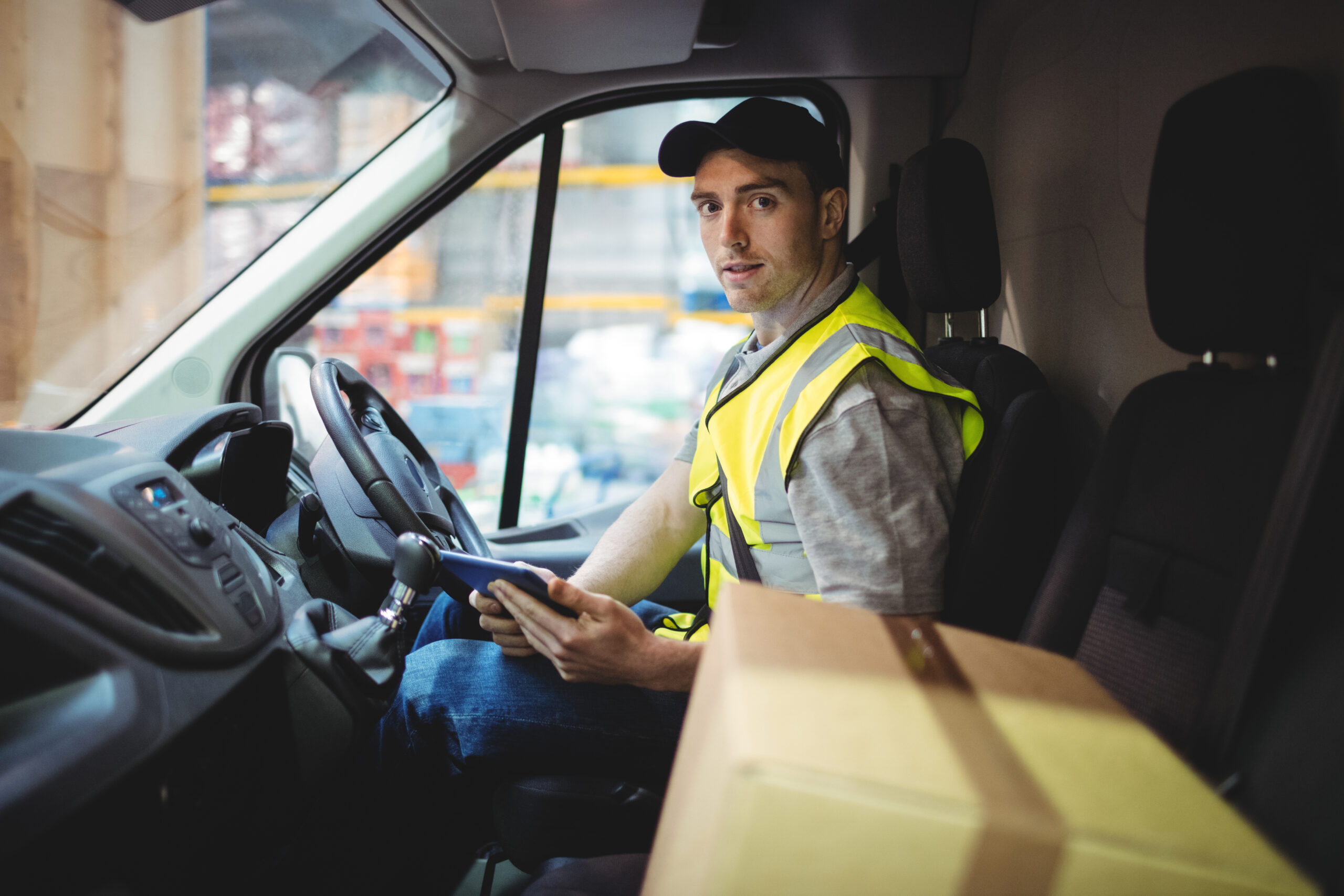 Delivery driver using tablet in van with parcels on seat