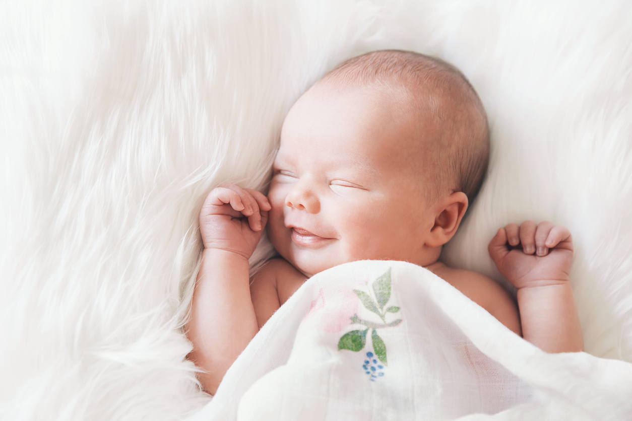 Sleeping newborn baby in a wrap on white blanket.