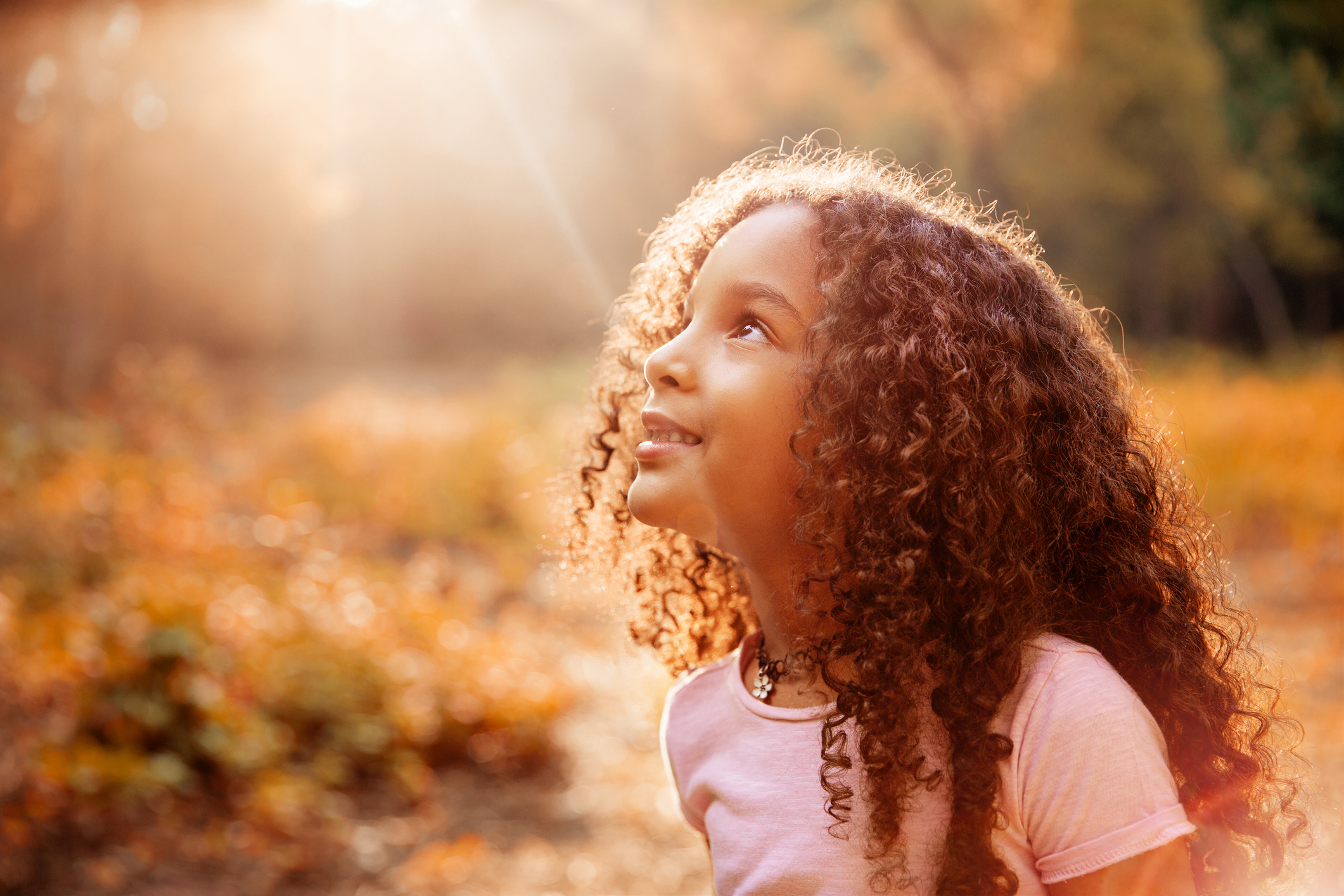 Afro american cute little girl with curly hair receives miracle sun rays from the sky