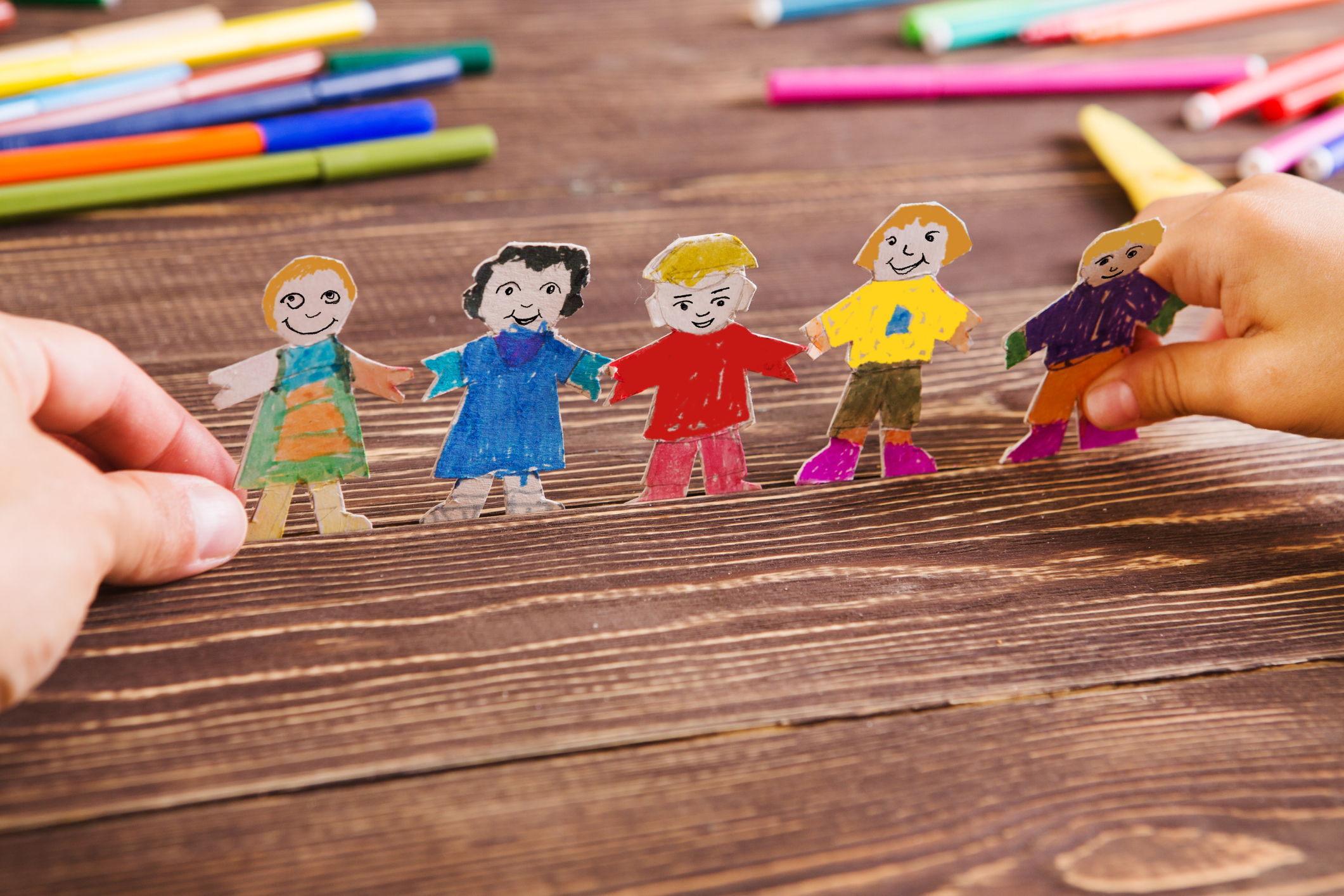 the child does figures of people of paper. Paper people on wooden background. Creative child play with craft.