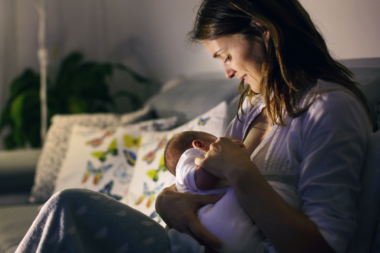 Young beautiful mother, breastfeeding her newborn baby boy at night