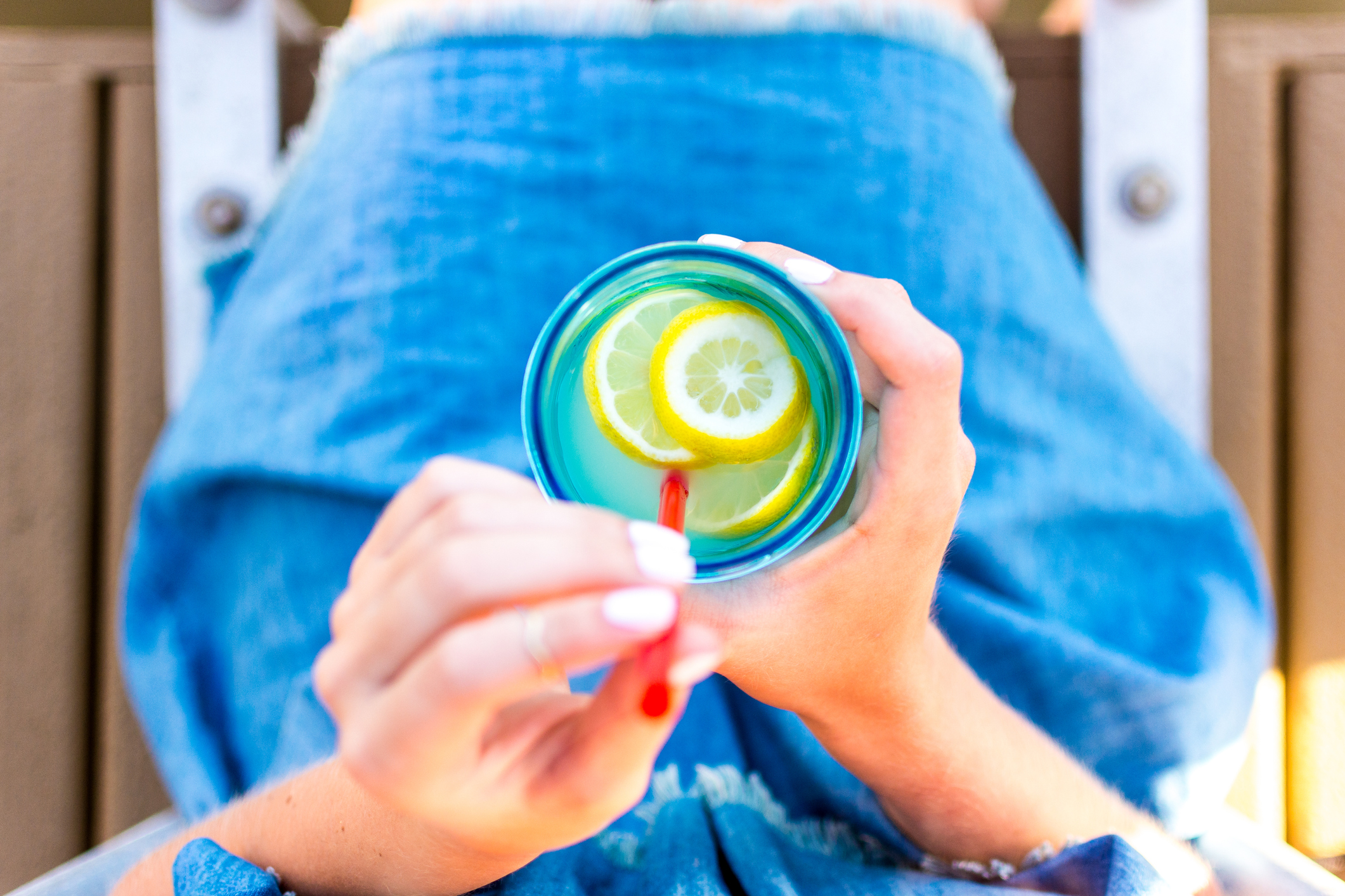 Girl Woman Holding a Mason Jar With Lemons Lemonade With a Red Straw on a Dock in a Blue Dress Point of View