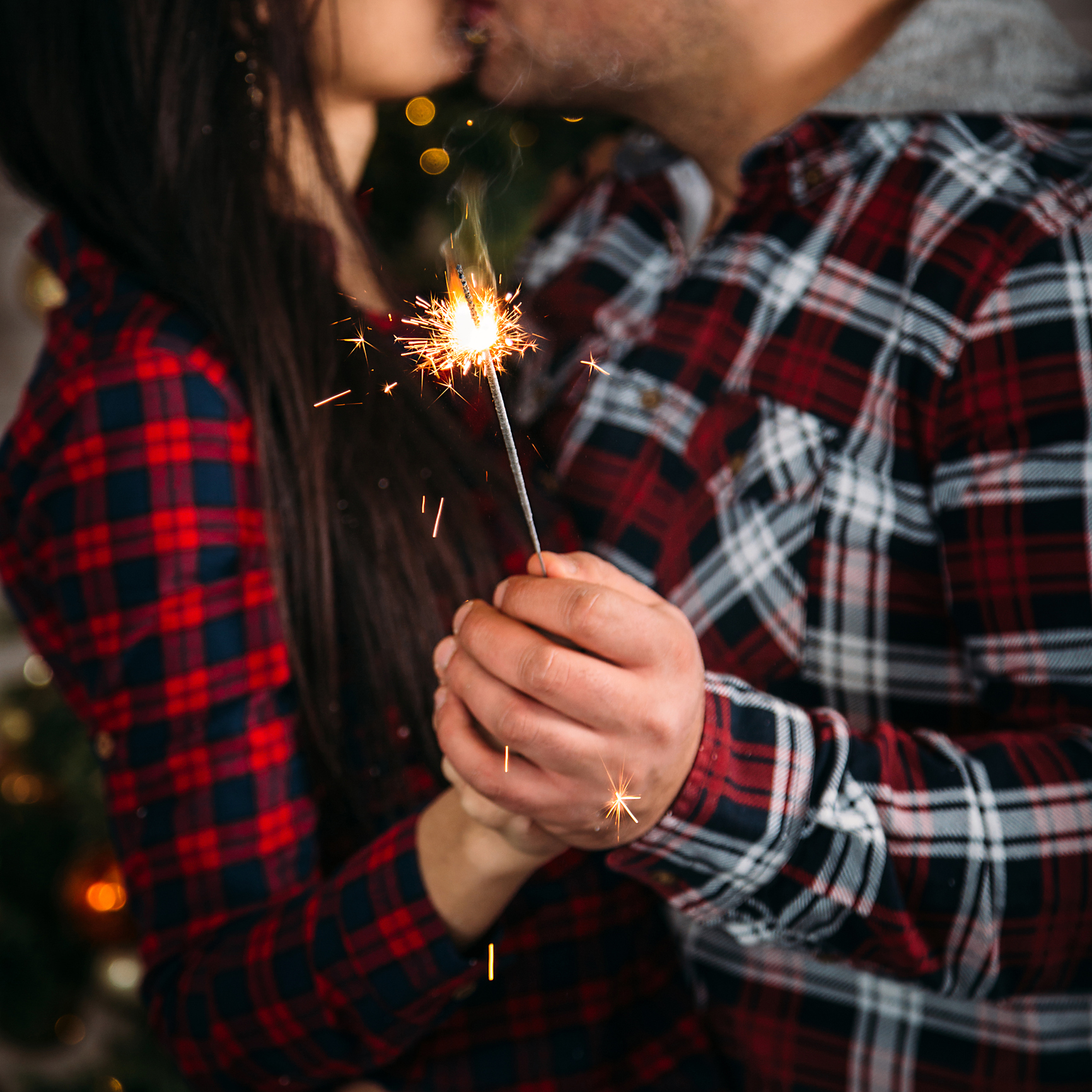 Christmas family portrait of young couple kissing and holding sparklers. Winter holiday Xmas and New Year concept