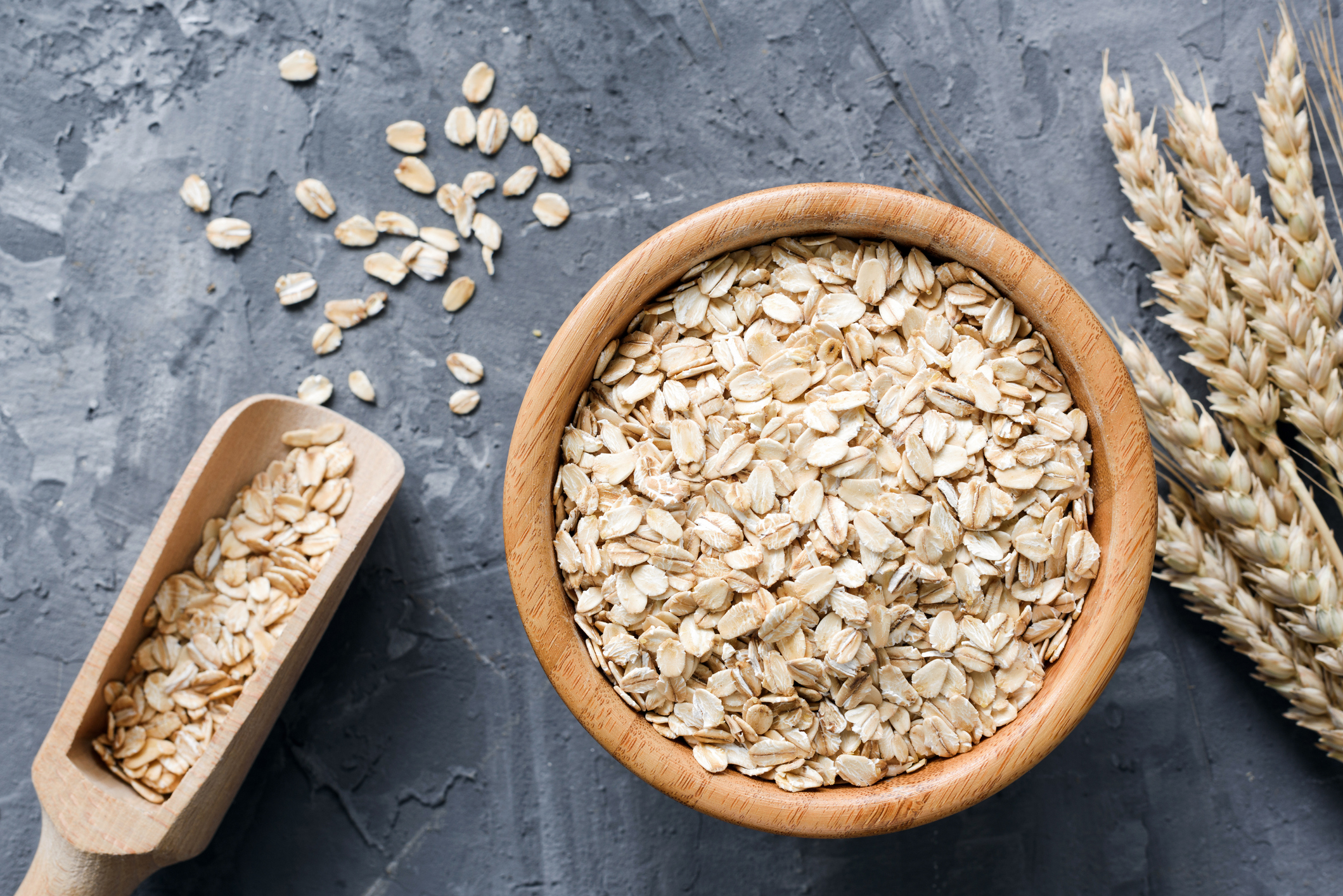 Rolled oats or oat flakes in wooden bowl on stone background.