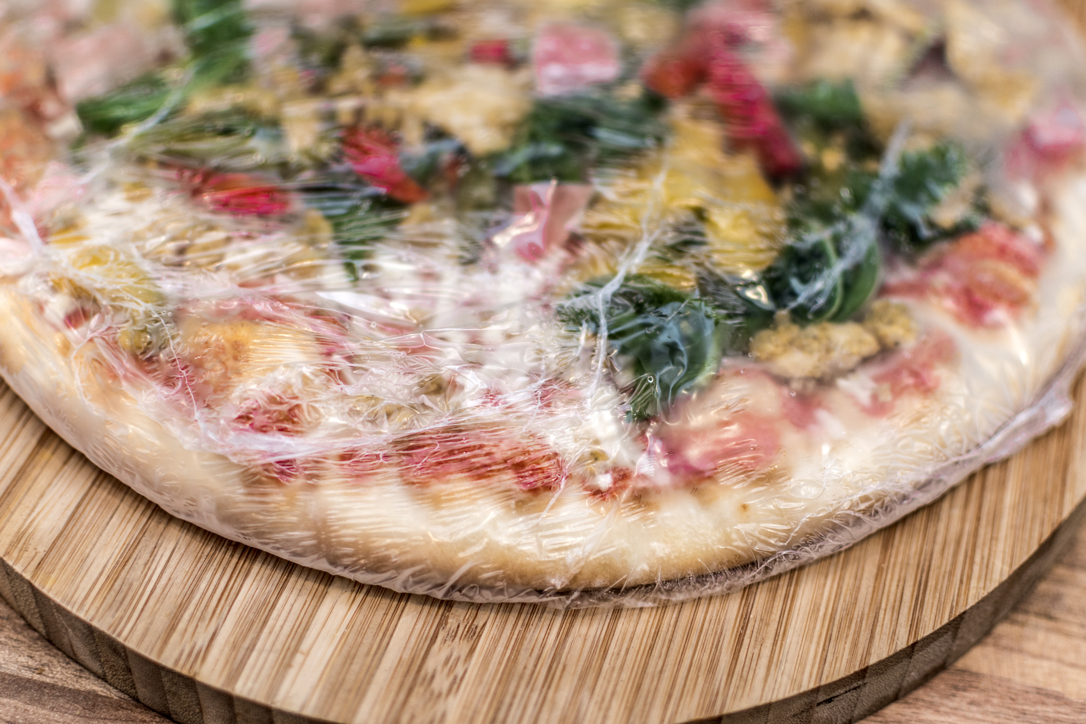 Frozen pizza still in plastic wrap on a board