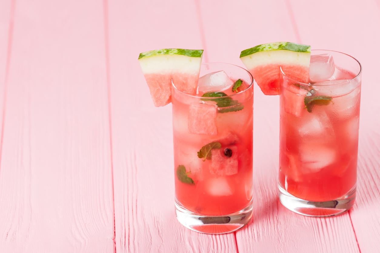 Watermelon lemonade with ice and mint leaves. Homemade lemonade of ripe berry with red and green ripes. Glass of cold watermelon tea. Refreshing summer drink. Cocktail on a wooden background