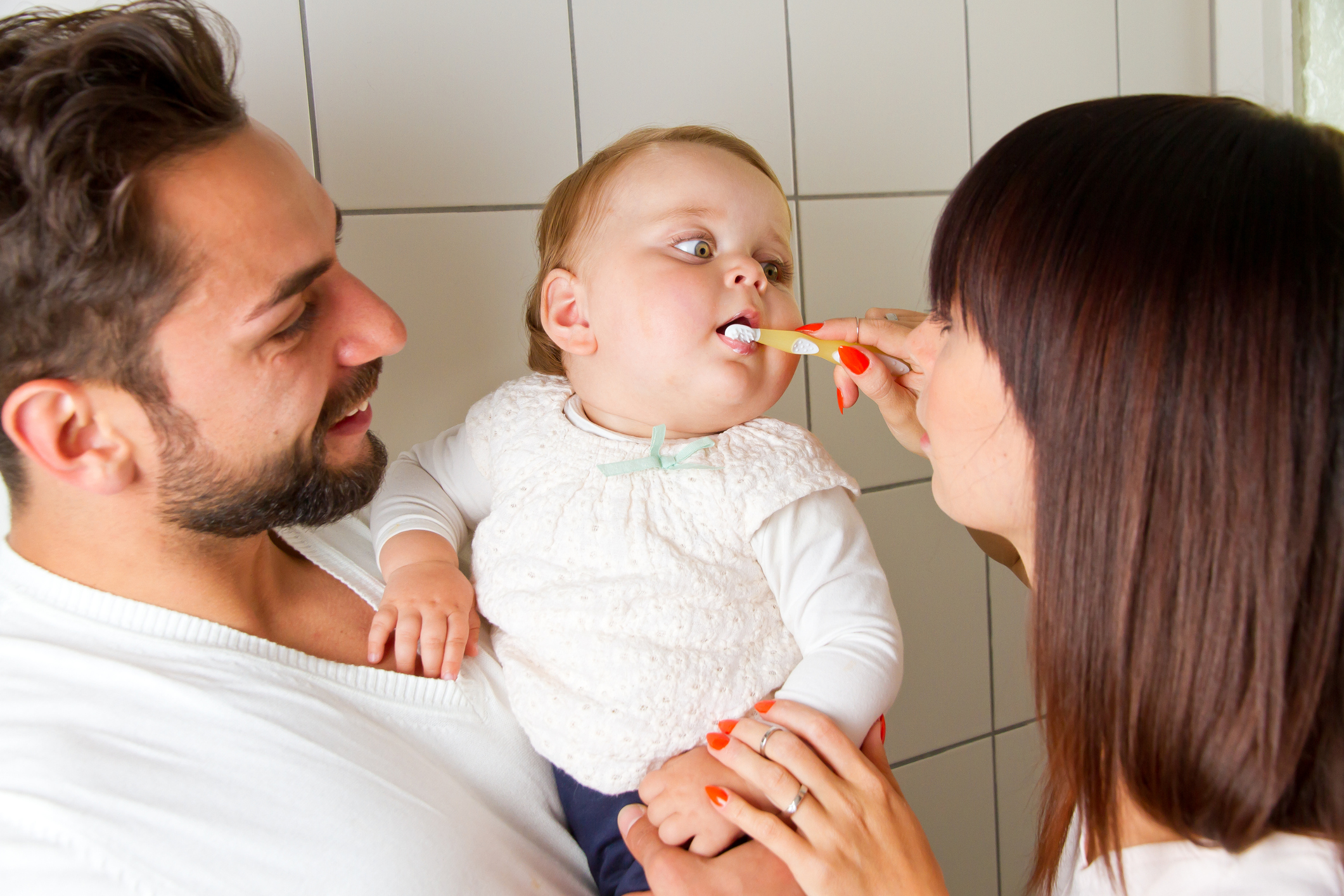 Mother and father brushing teeth of their baby