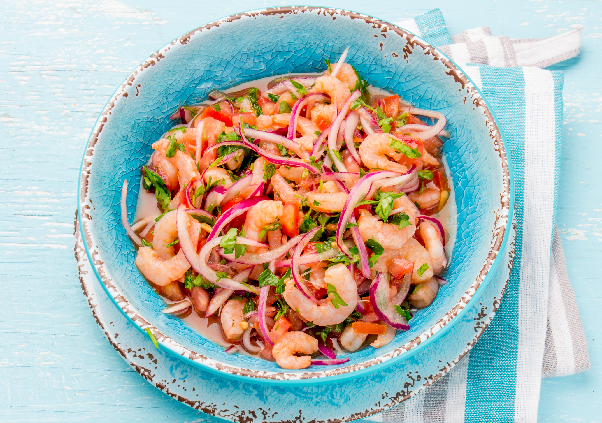 Ecuadorian shrimps ceviche sebiche with tomatoes in blue bowl, wooden blue background. Traditional ecuadorian colombian or mexican dish.