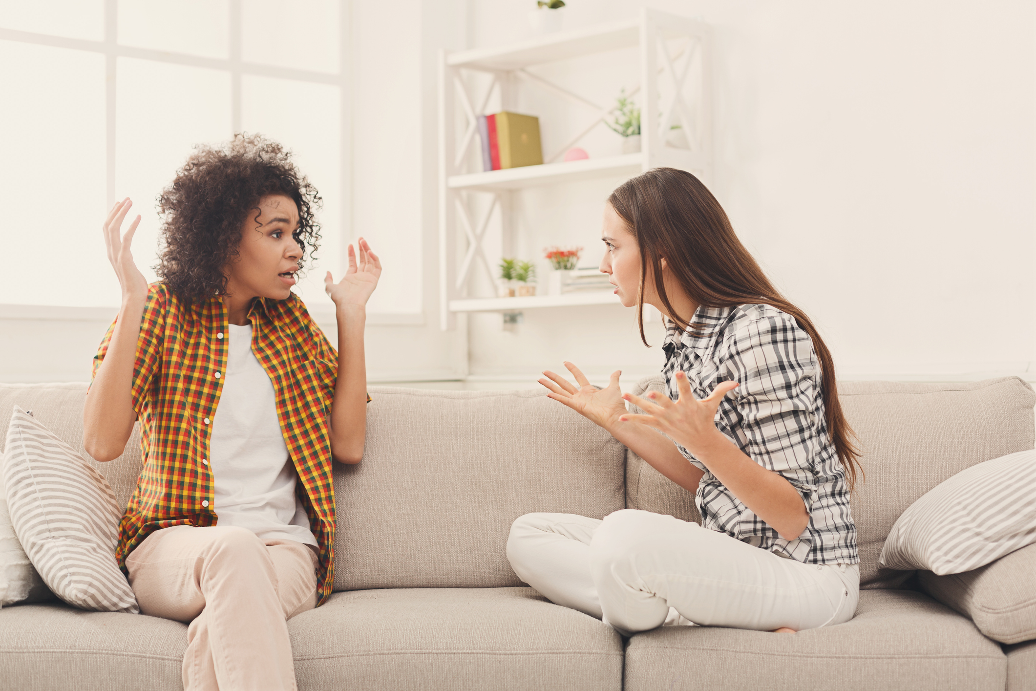 Two female friends sitting on sofa and arguing