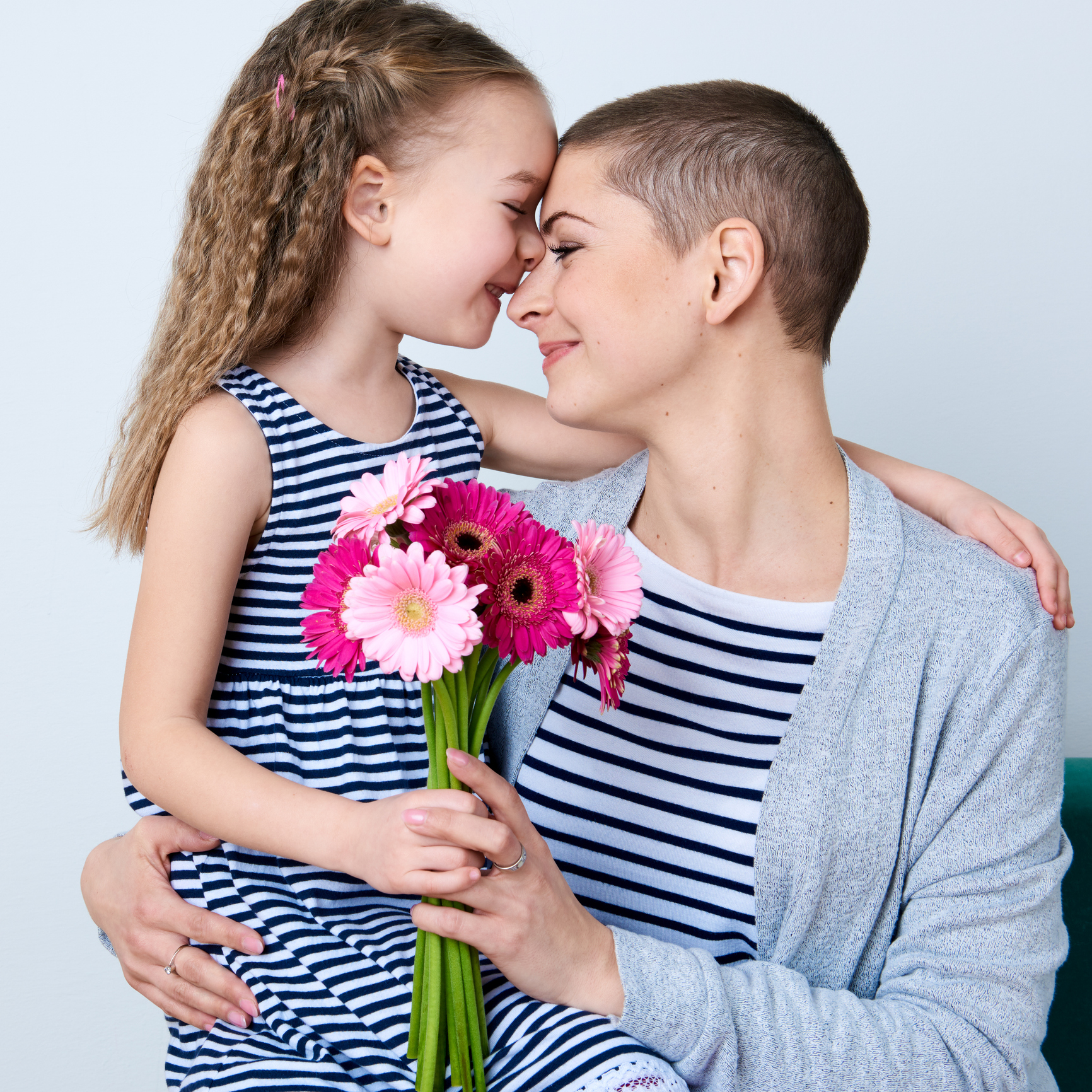 Happy Mother's Day, Women's day or Birthday background. Cute little girl giving mom bouquet of pink gerbera daisies. Loving mother and daughter smiling and hugging.