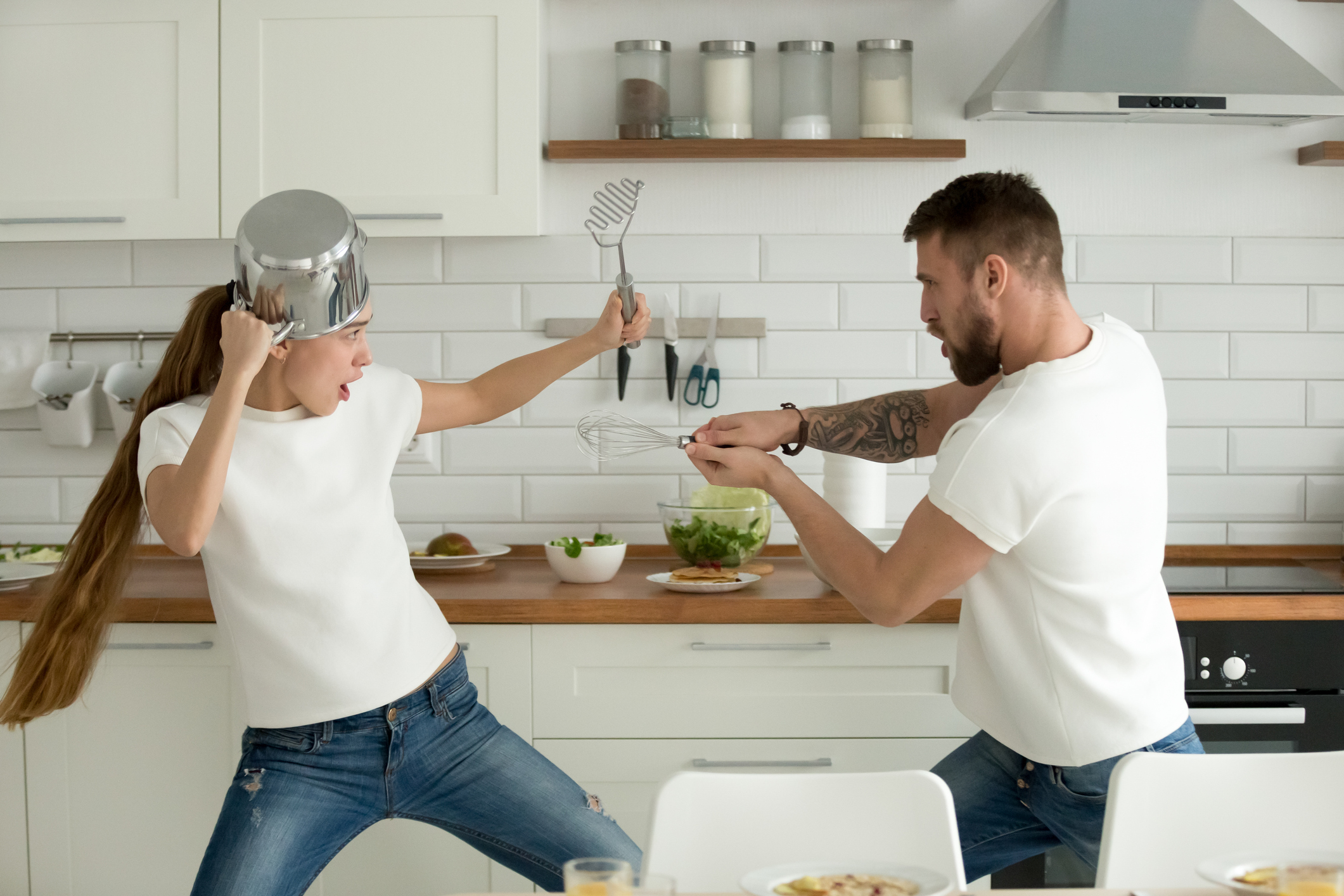 Funny couple having fun fighting with kitchen utensils cooking t