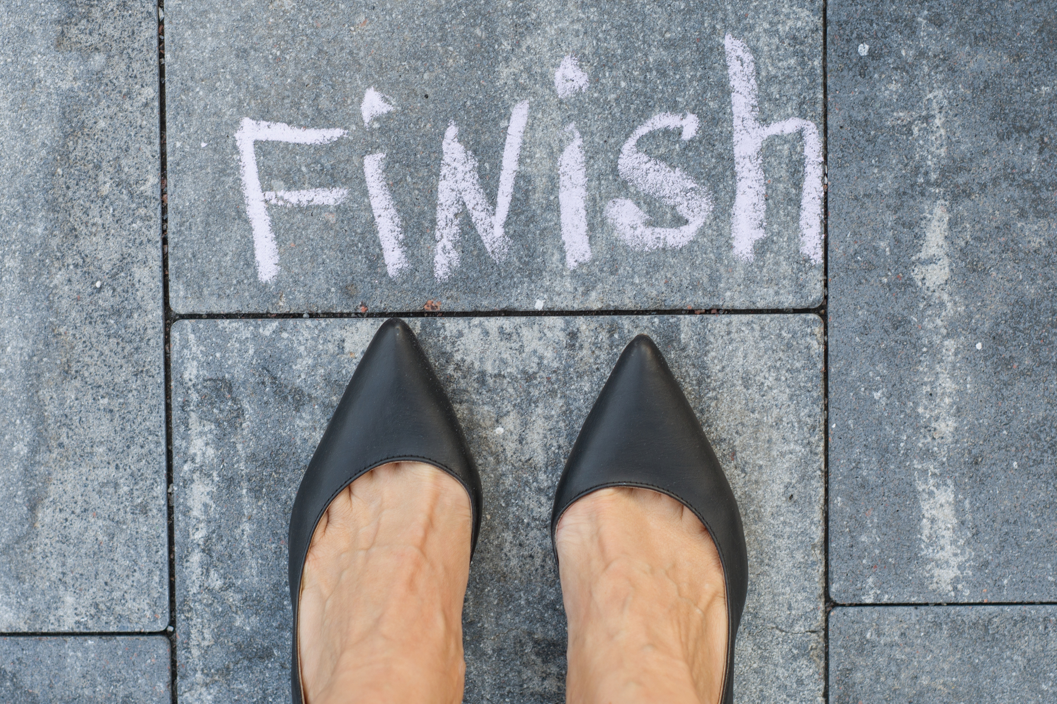 The feet of a woman in black classic shoes before the word finis