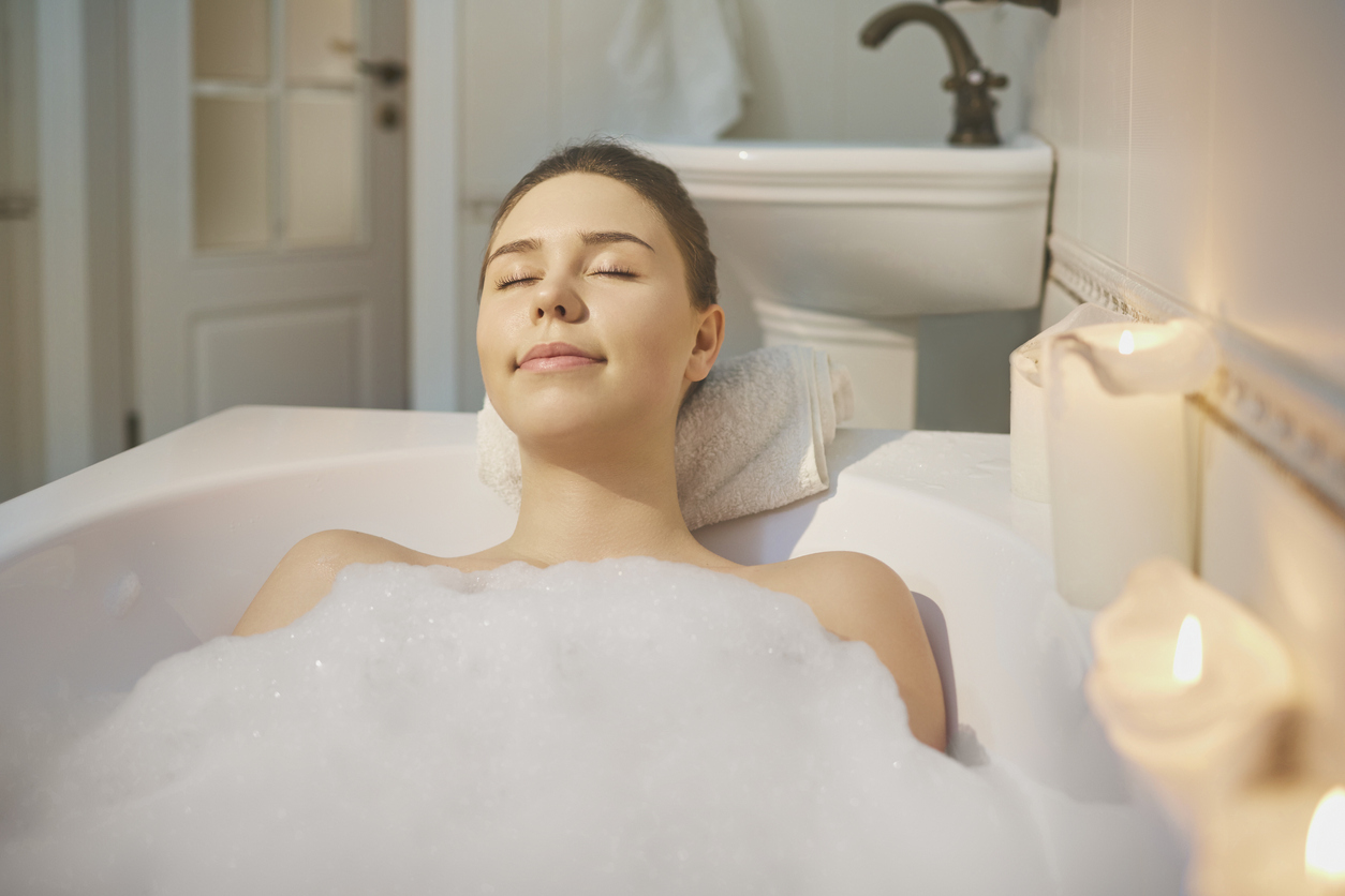 Young girl is resting in a bathtub with foam  with candle