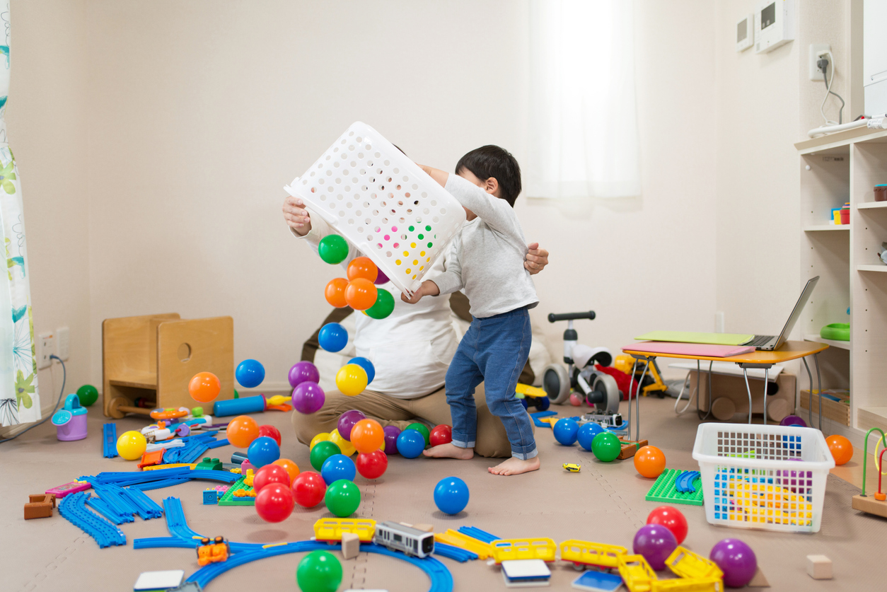 Pregnant mother and toddler playing together with toy in untidy room