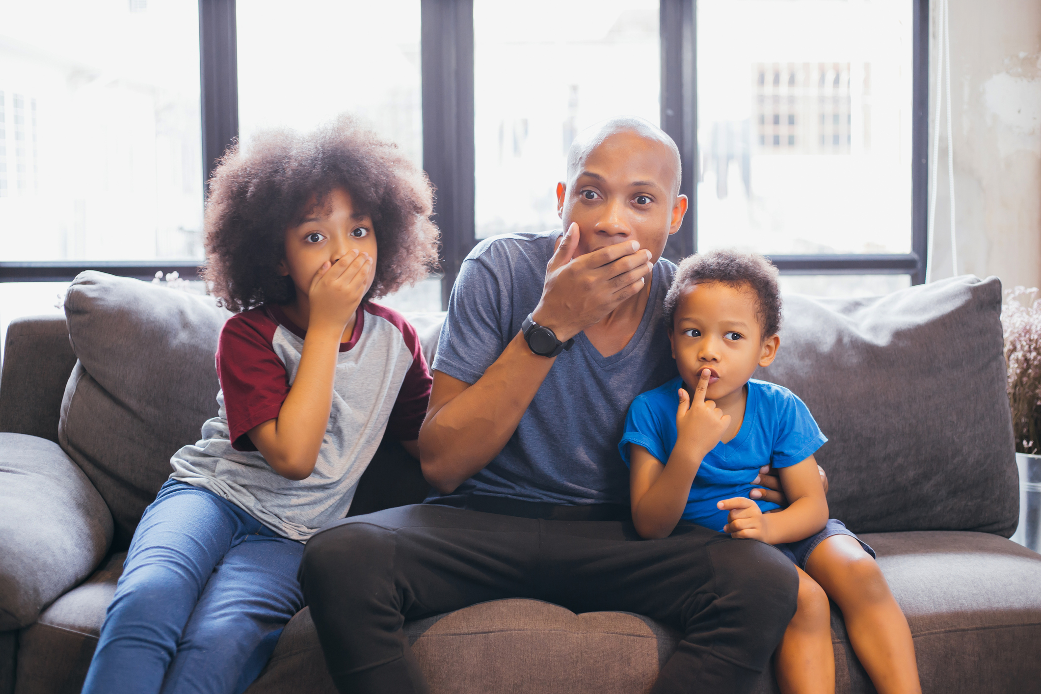 Whole family of African American watching and staring horror movie on TV at home. They are getting frightened and scared.