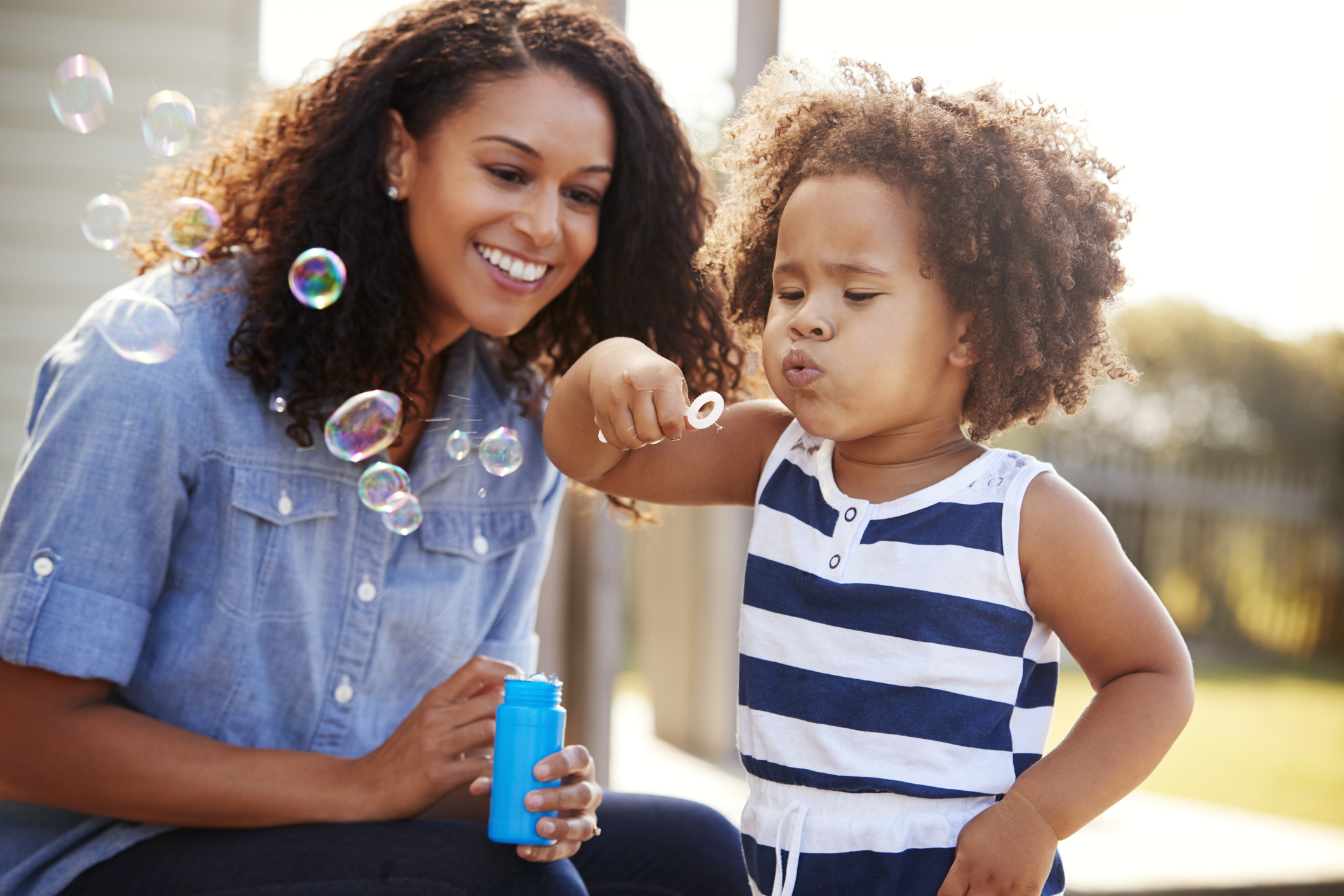 Young mixed race mother and daughter blowing bubbles outside