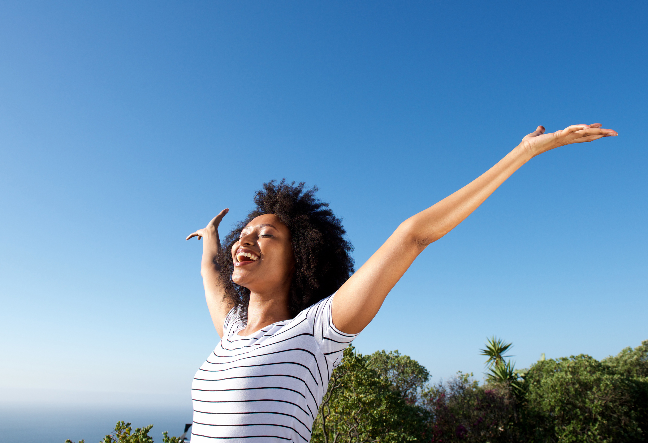 young african woman standing outdoors with arms raised and laughing