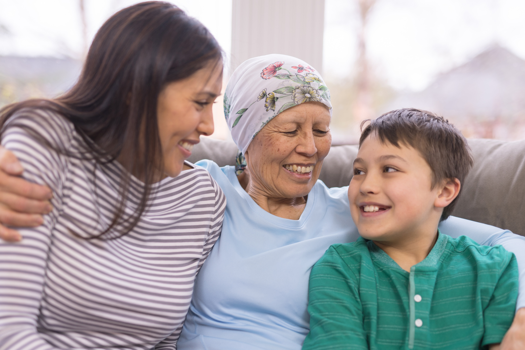 Happy ethnic woman with cancer embraces her adult daughter and grandson